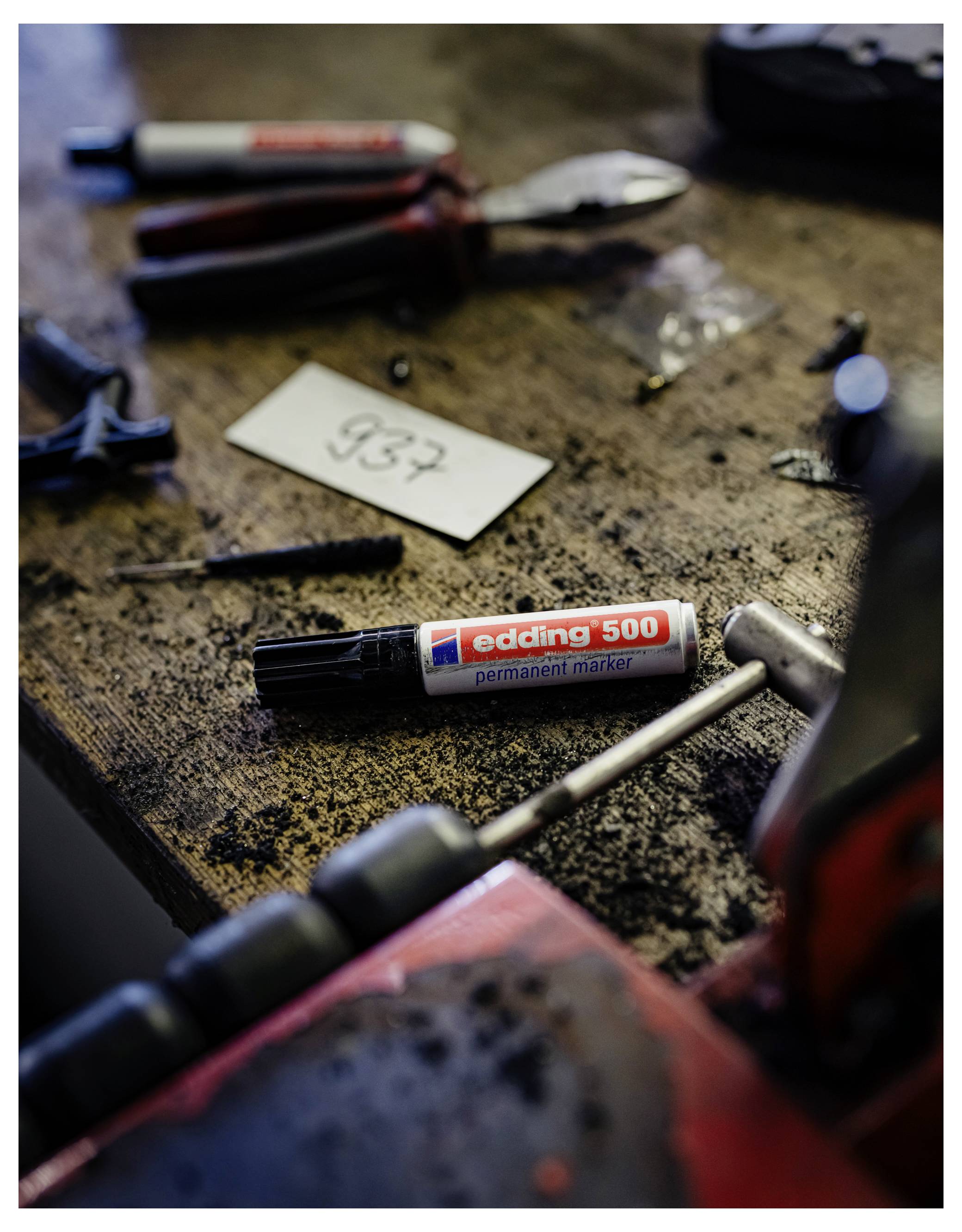 Eine unordentliche Werkbank mit Handwerkzeugen, einem Permanentmarker mit der Beschriftung „edding 500" und einer kleinen Karte mit der Nummer „937".