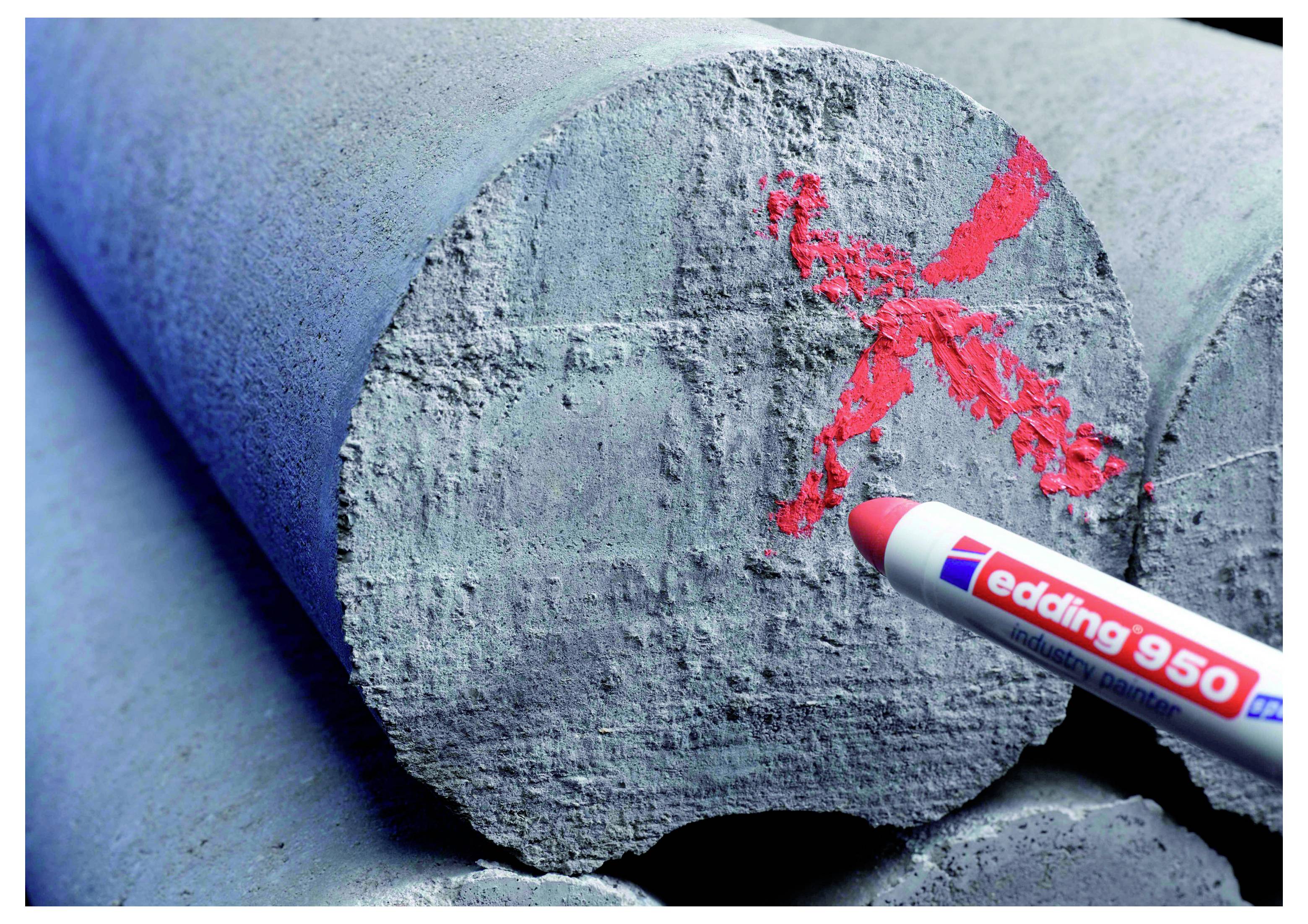 Nahaufnahme einer Hand, die mit einem roten Marker ein X auf die ebene Oberfläche eines großen Betonzylinders zeichnet.