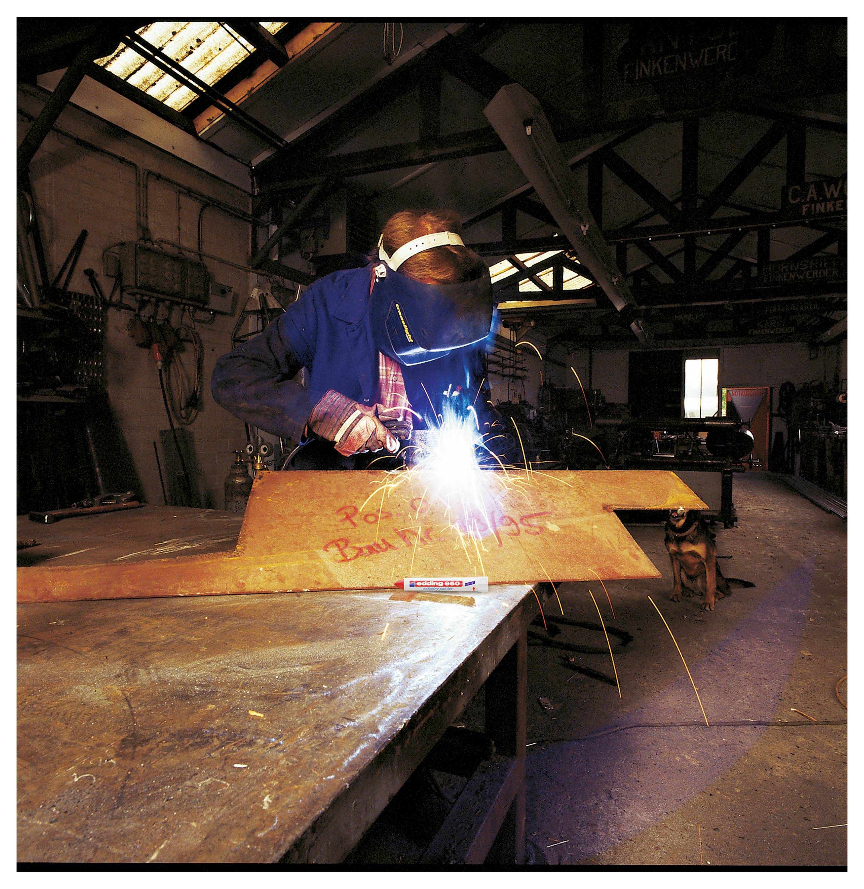 Ein Schweißer in einer Werkstatt verbindet Metall mit einem hellen Lichtbogen und Funken und trägt dabei einen Schutzhelm und Handschuhe.
