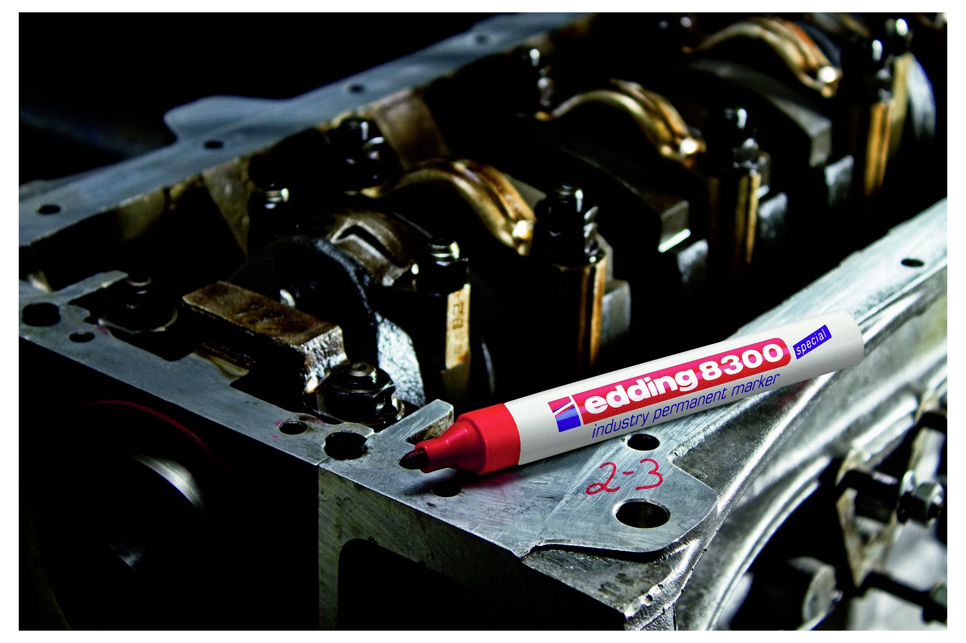 Roter Edding 8300 Industrie-Permanentmarker, der auf einem Metallteil eines Motors ruht, mit roter handschriftlicher Beschriftung "2-3" auf der Oberfläche.