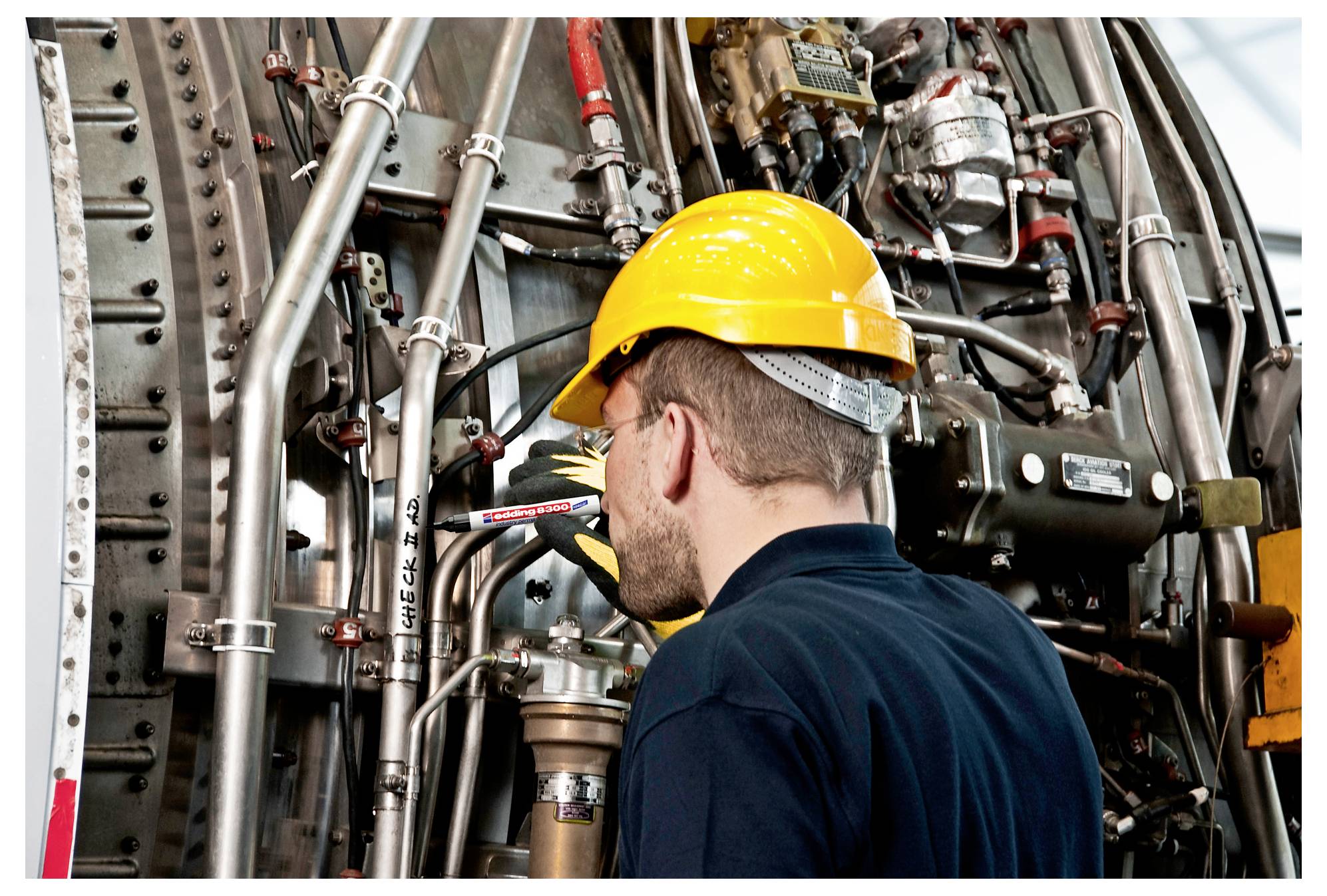 Arbeiter in einem gelben Schutzhelm inspiziert dichte Industrierohre und Maschinen in einer Anlage.