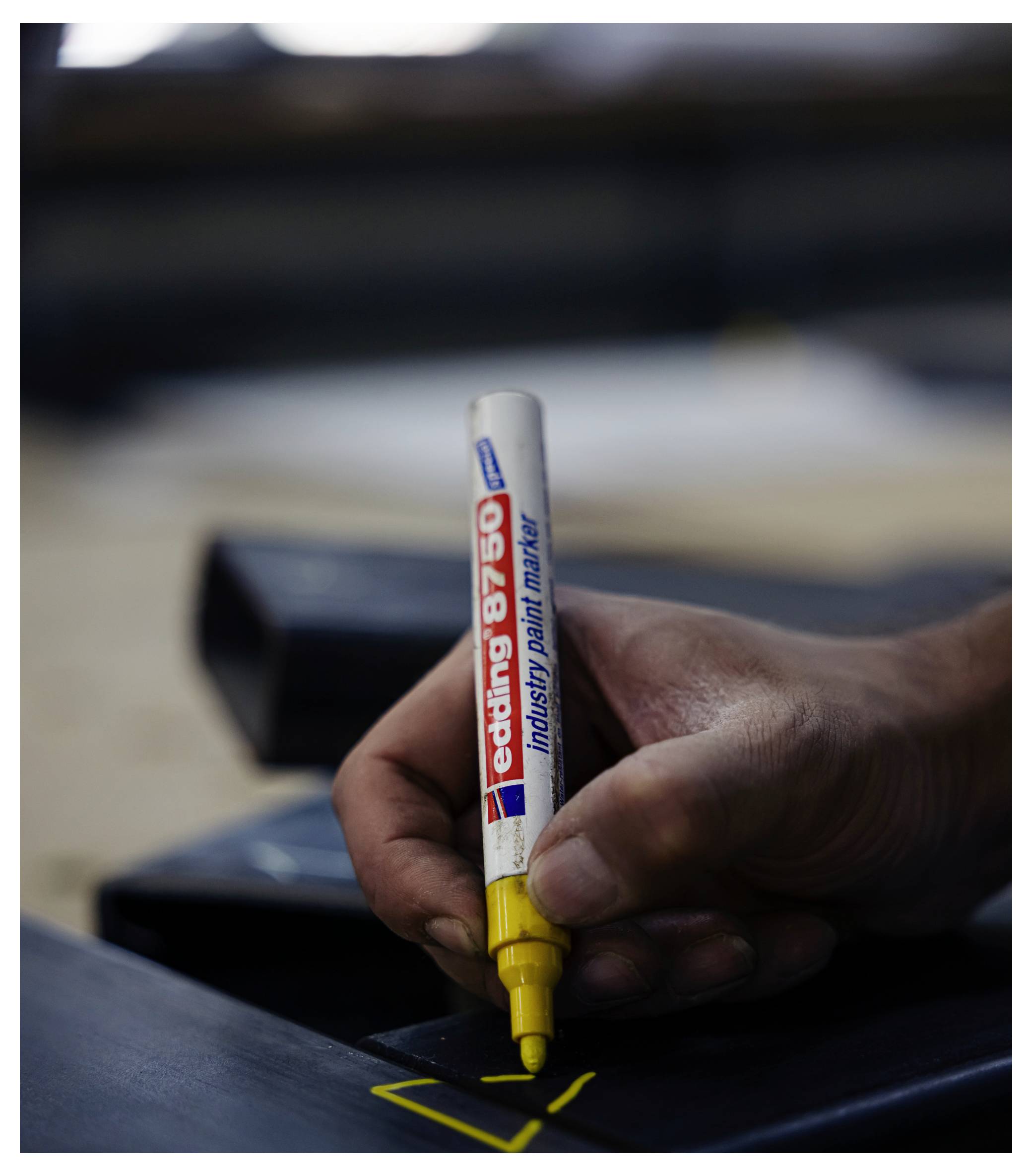 Hand hält einen gelben Industrie-Lackstift und markiert eine schwarze Oberfläche mit einer gelben Linie.