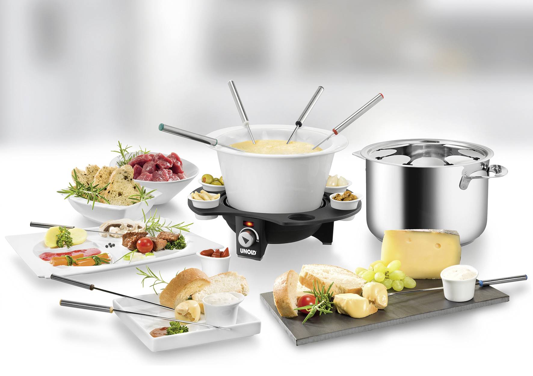 Fondue-Set mit verschiedenen Zutaten: Käse, Brot, Fleisch, Kartoffeln, Gemüse auf Tellern; Elektrokochplatte mit Fondue-Topf.
