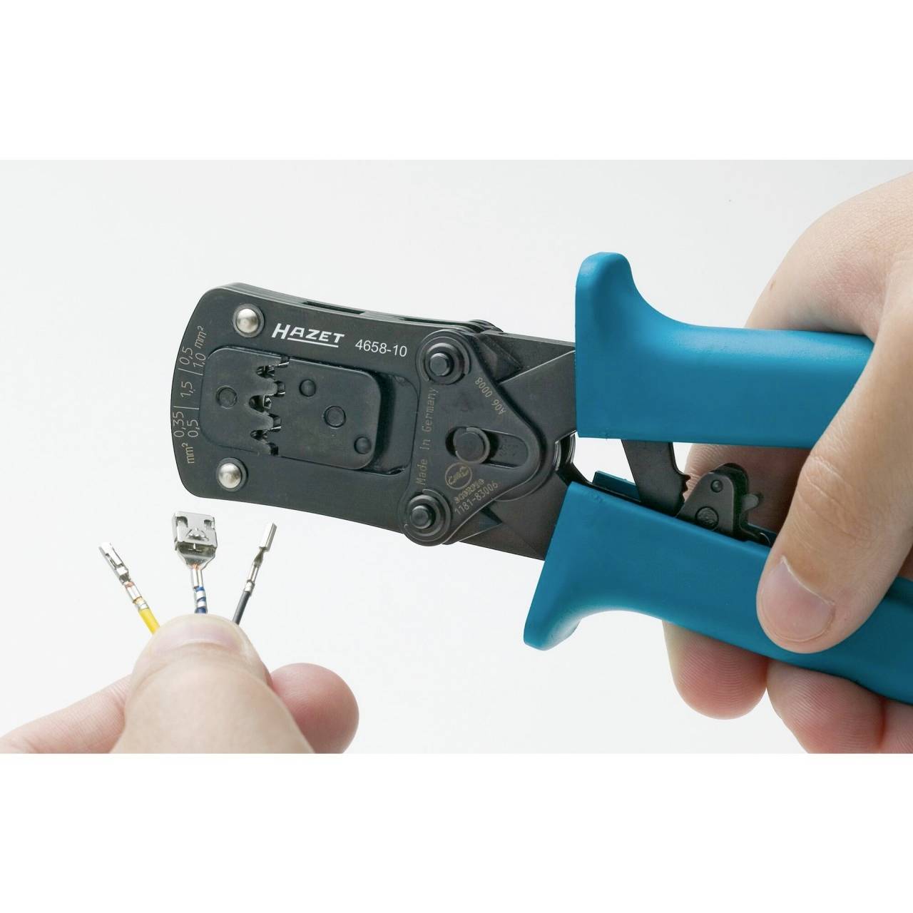 Eine Hand hält eine blaue Crimpzange der Marke Hazet, die dabei ist, Kabelschuhe an einem Kabel zu befestigen.