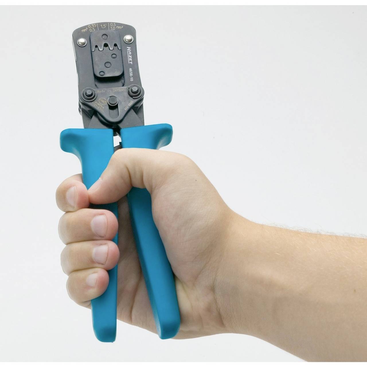 Eine Hand hält eine Crimpzange mit blauen Griffen. Die Zange wird für Kabelverbindungen verwendet und liegt fest in der Hand.