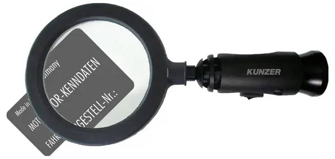 Eine Lupe zeigt Text auf einem kleinen Schild mit schwachen Details. Der Griff ist mit 'Kunzer' beschriftet.