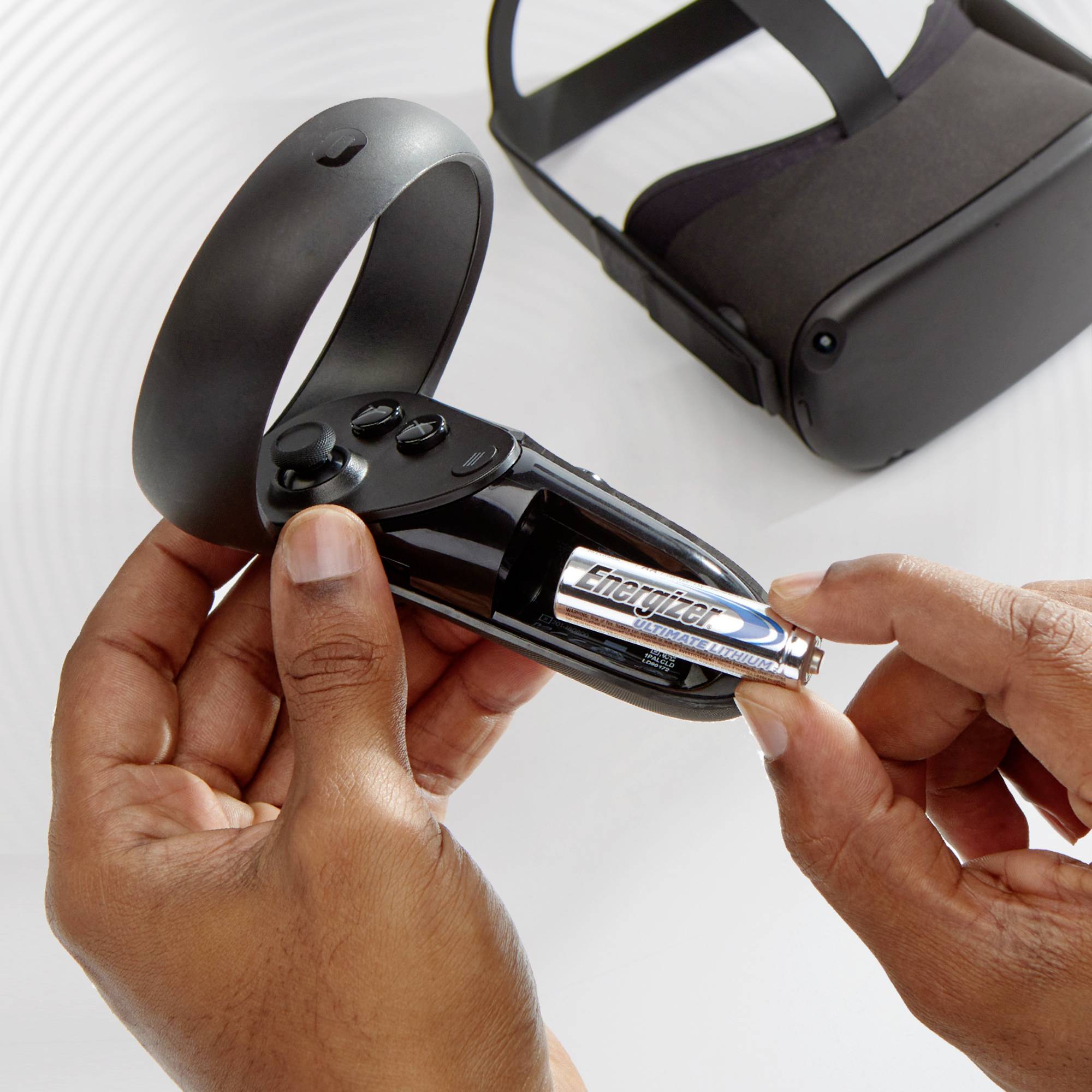Eine Person hält eine VR-Controller-Fernbedienung und setzt eine AA-Batterie ein. Eine VR-Brille liegt im Hintergrund.