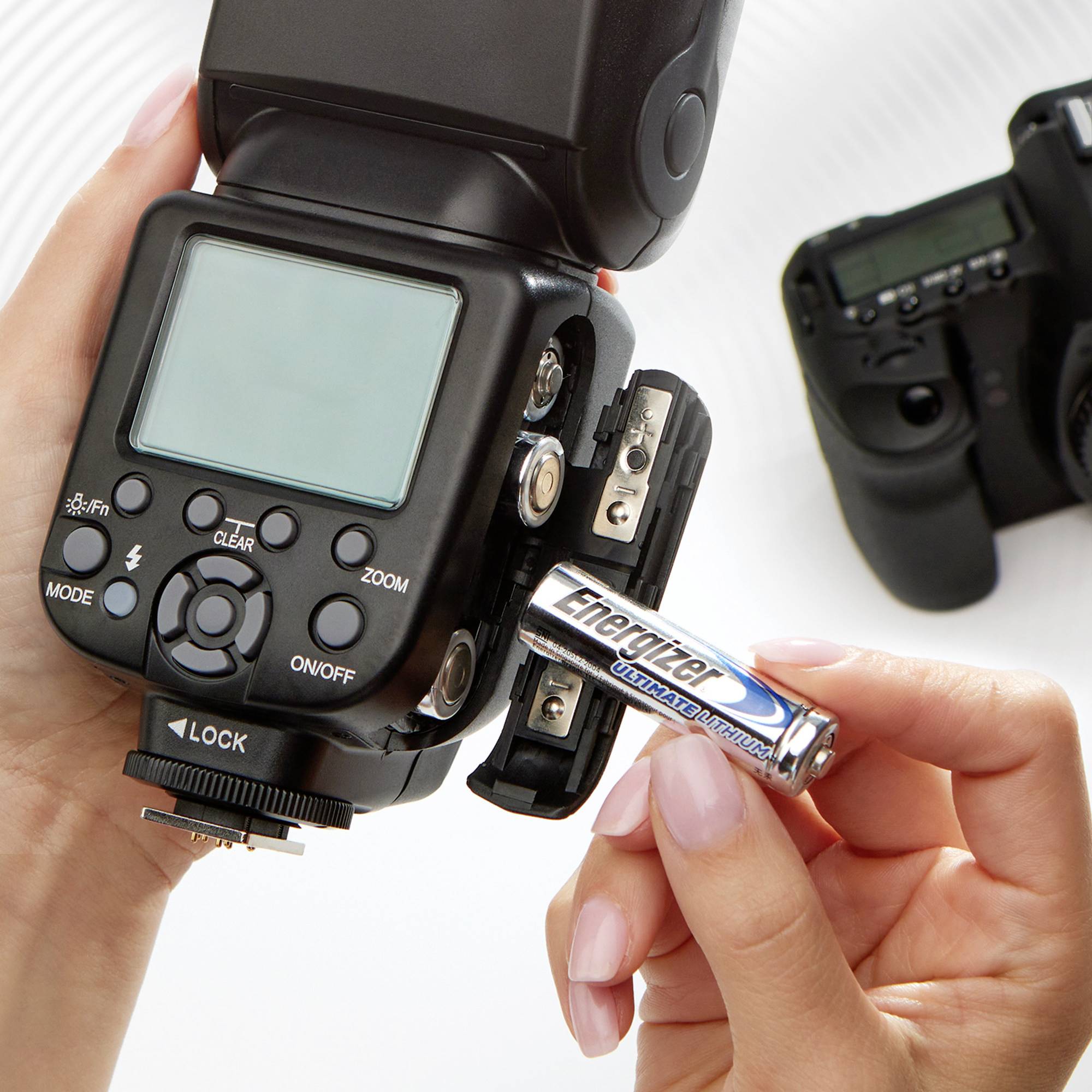 Eine Person hält eine Energizer-Batterie bereit, um einen DSLR-Kamerablitz zu laden. Im Hintergrund liegt eine Kamera auf einem Tisch.