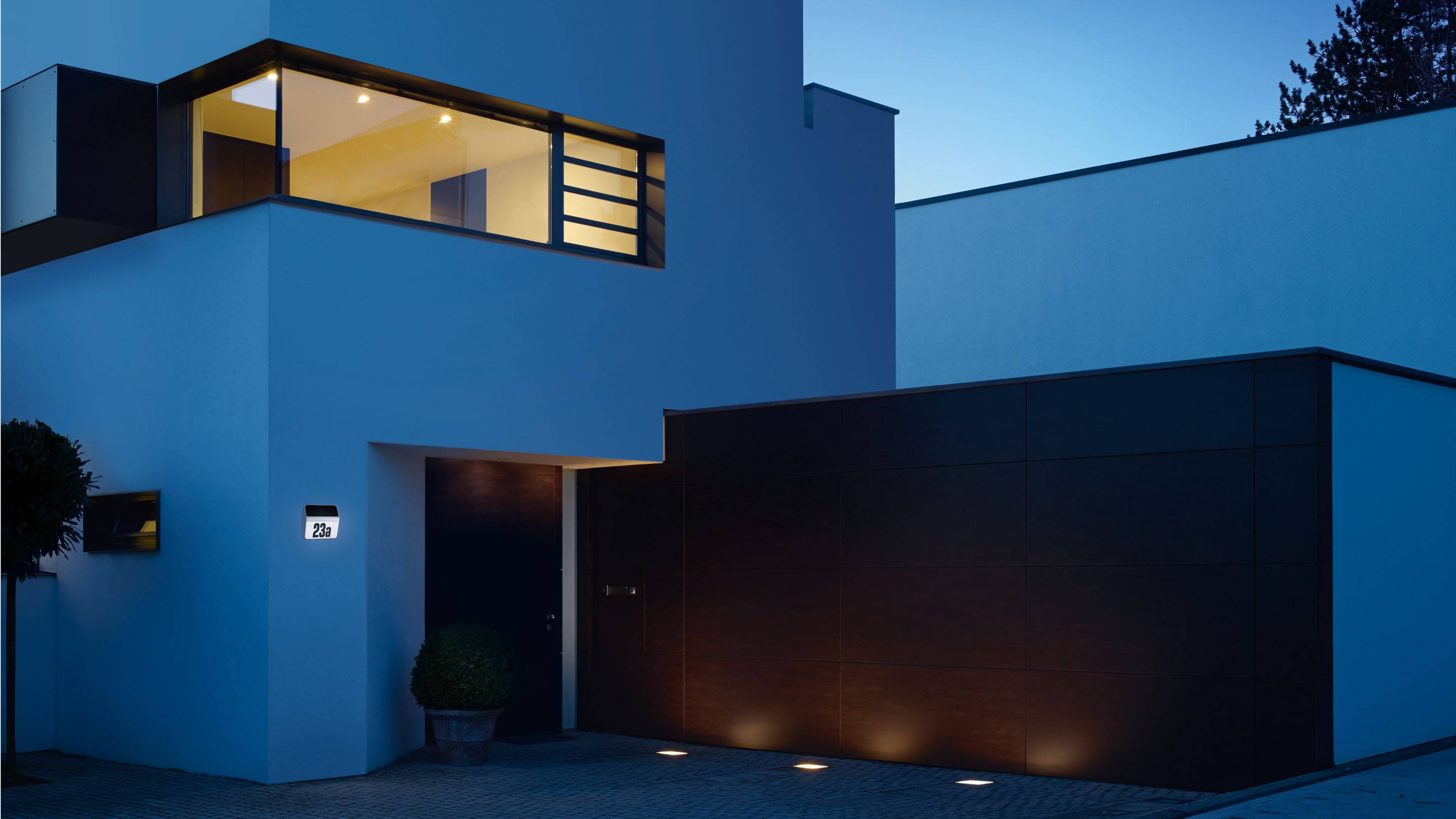 Moderne, weiße Villa bei Nacht mit beleuchteten Fenstern und Eingangsbereich. Elegantes, minimalistisches Design mit klaren Linien.
