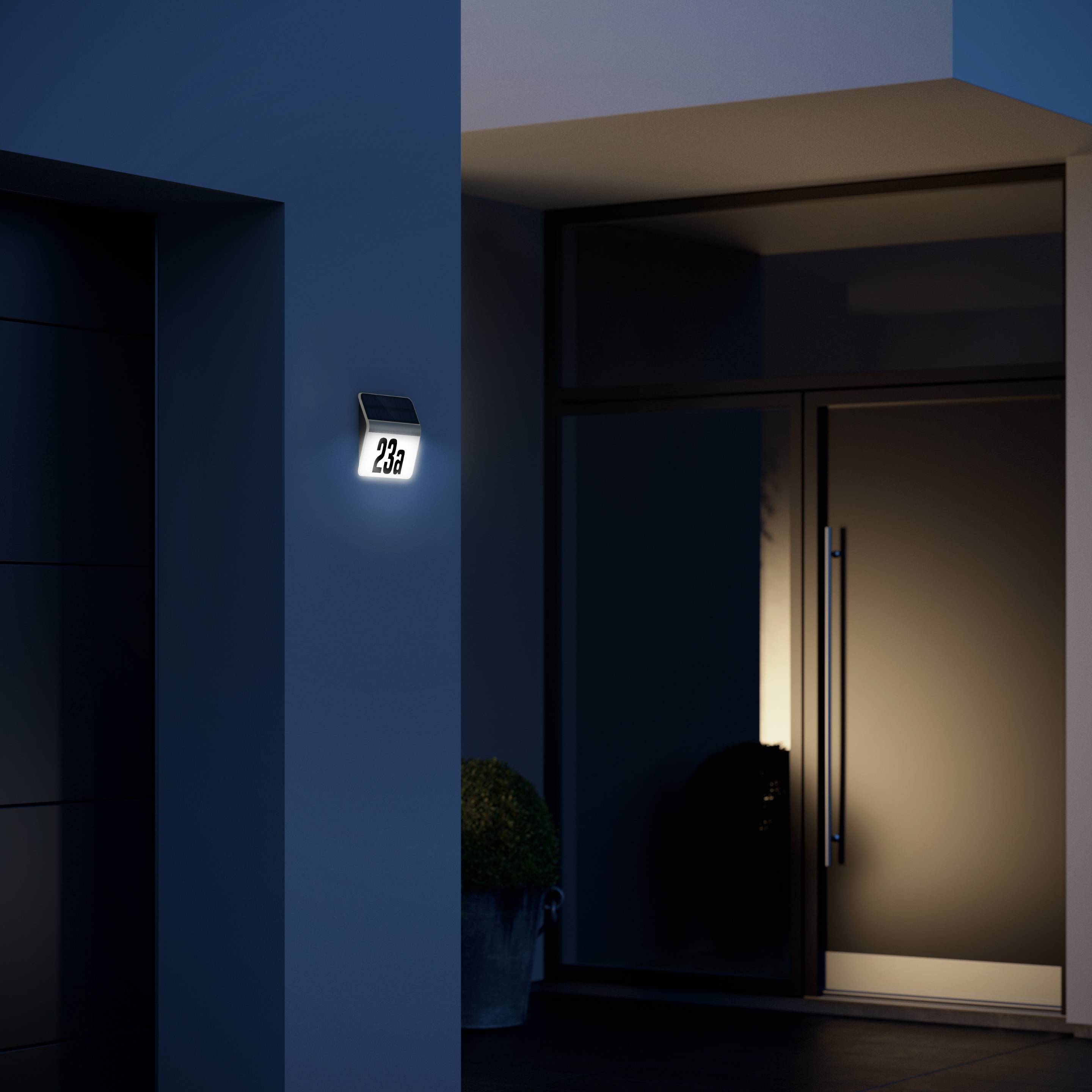 Eine moderne Außenansicht eines Hauses bei Nacht, erleuchtete Hausnummer '23a', mit einem großen Glasfenster und einer Tür.