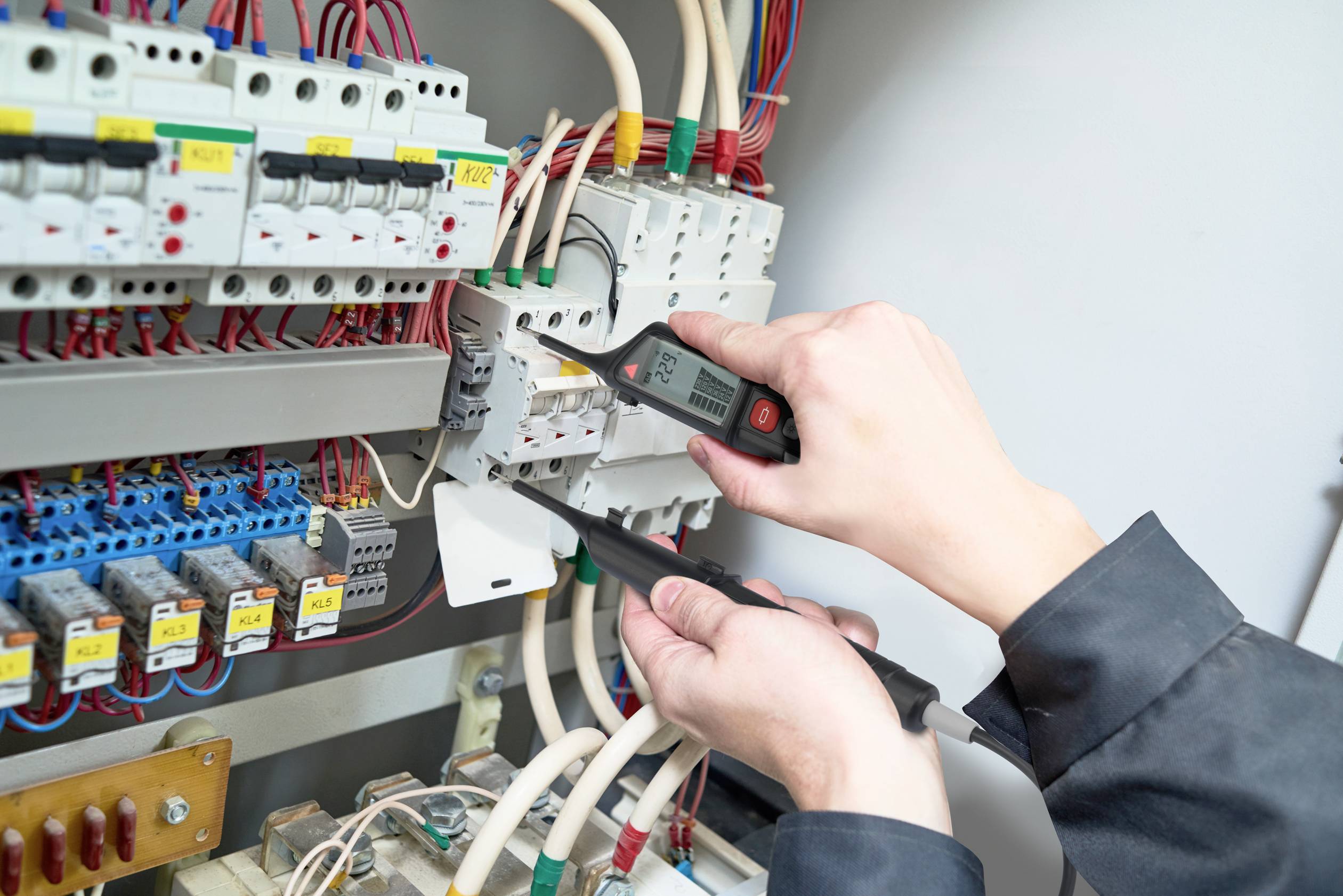 Eine Person prüft mithilfe eines Testgeräts elektrische Sicherungen in einem Verteilerkasten. Die Szene zeigt Sorgfalt und Technik.