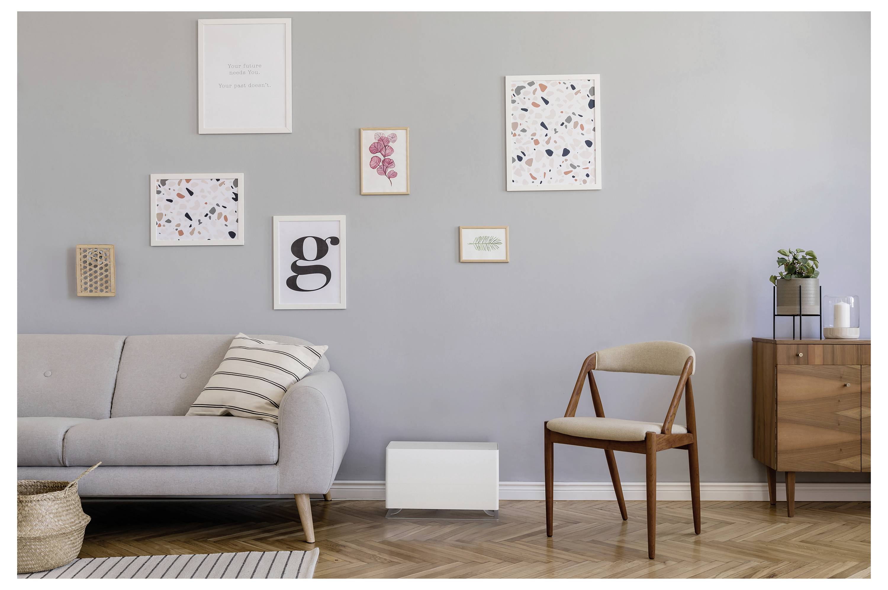 Modernes Wohnzimmer mit grauem Sofa, gestreiftem Kissen, Holzstuhl, kleinem Schrank und gerahmtem Wandbild an einer hellgrauen Wand.
