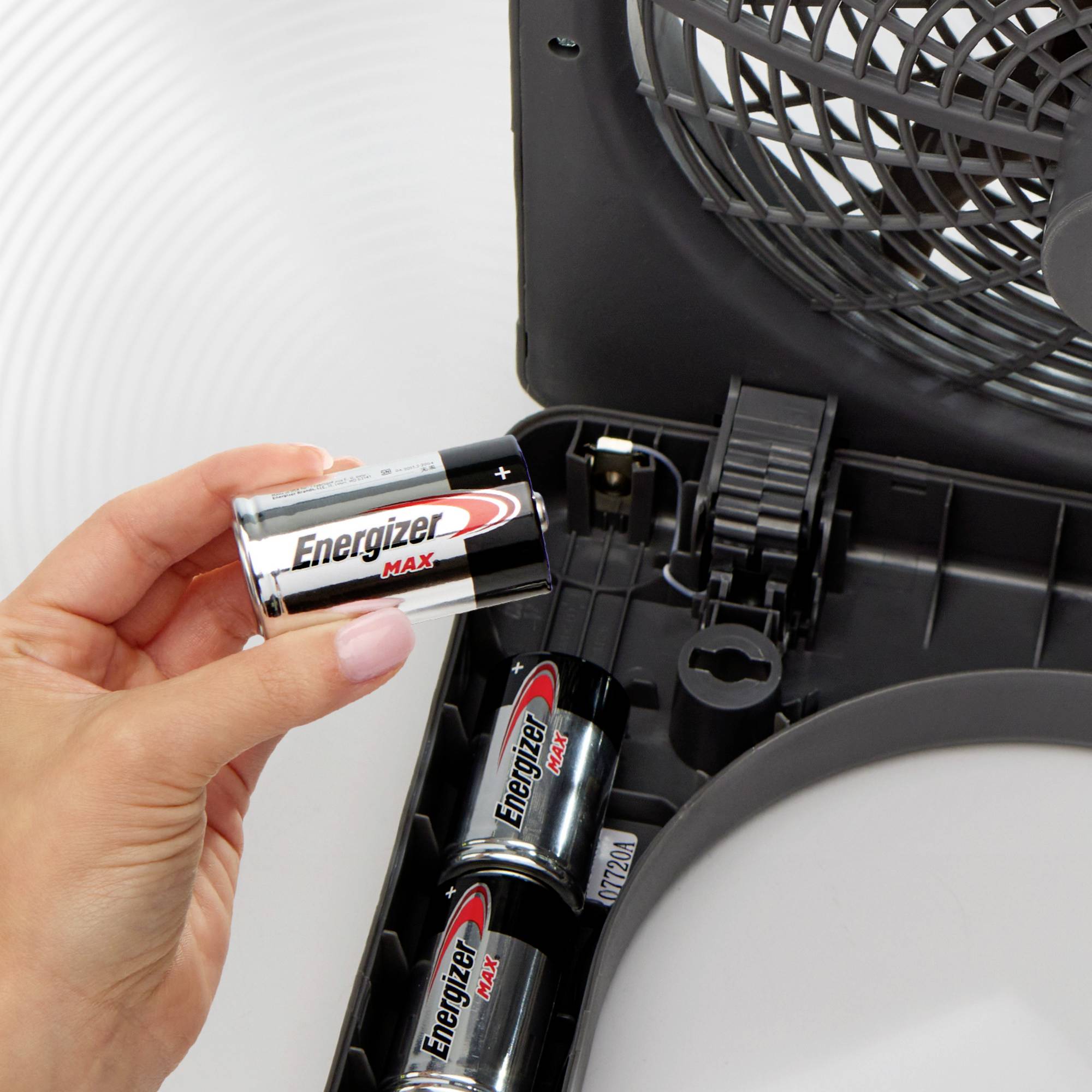 Eine Person setzt eine AA-Batterie mit dem Schriftzug 'Energizer Max' in ein Batteriefach ein. Im Hintergrund sind weitere Batterien.