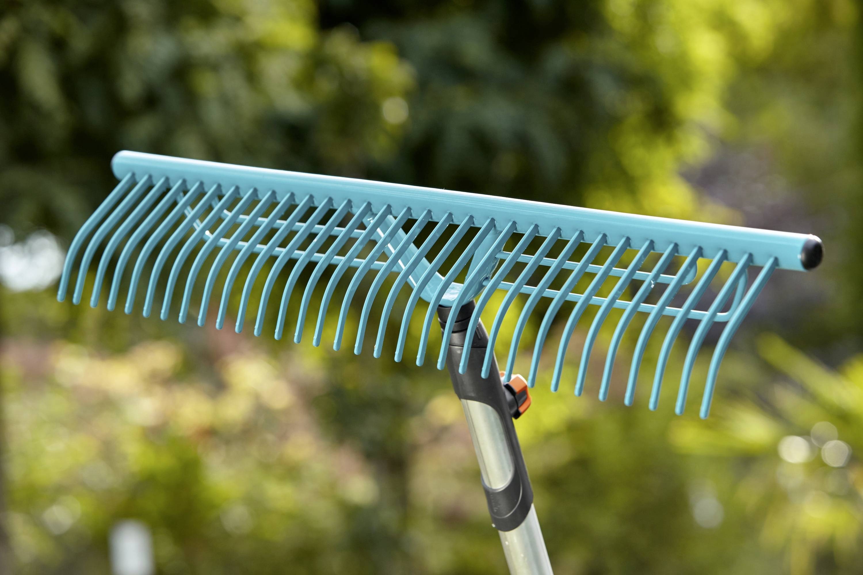 Ein blauer Laubrechen vor einem verschwommenen grünen Hintergrund, bereit zum Harken von Blättern oder Gartenabfällen.