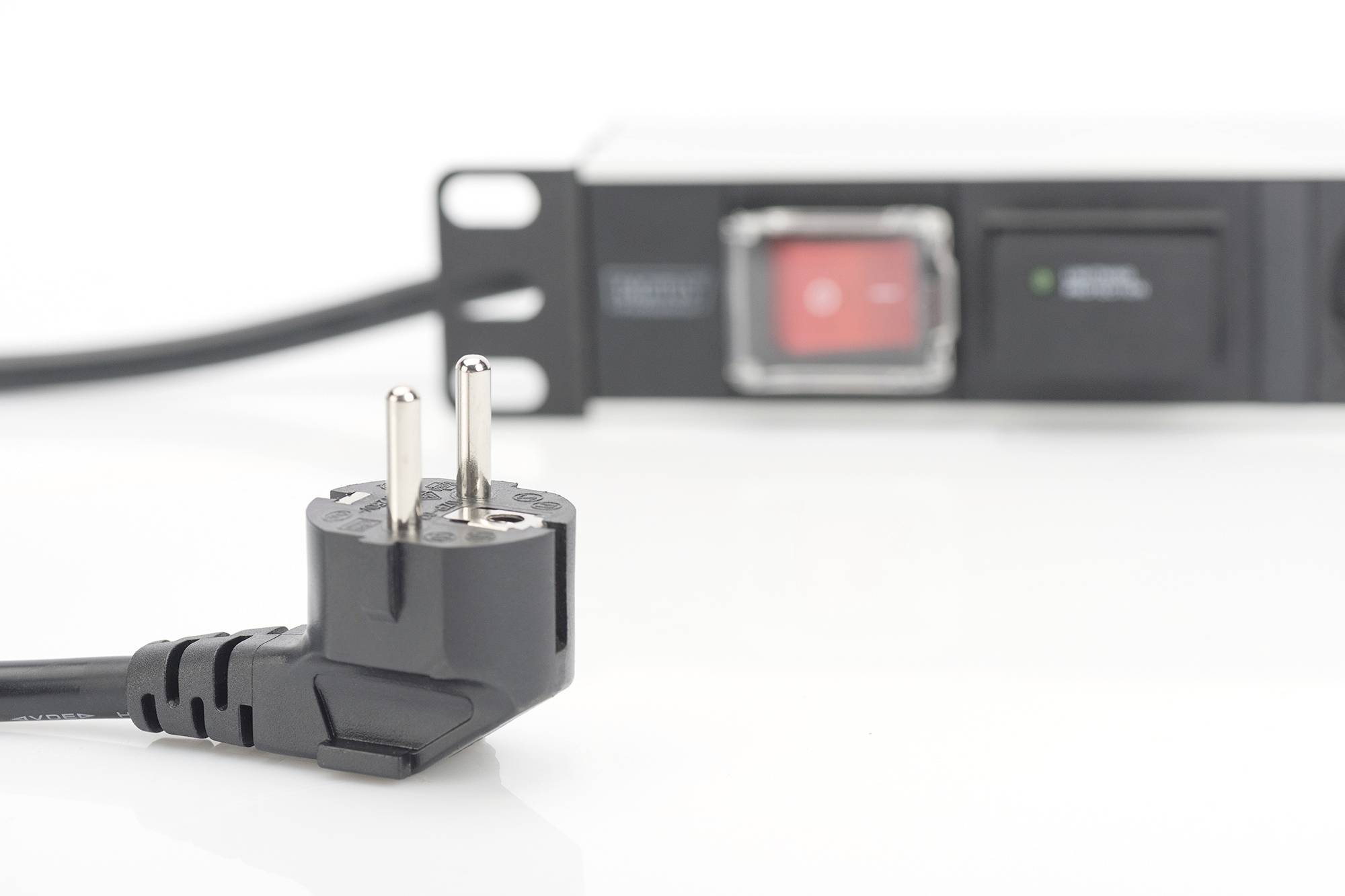 Ein schwarzer Eurostecker liegt im Vordergrund, unscharf dahinter ist ein Rack-Power-Management-Modul mit Schalter zu sehen.