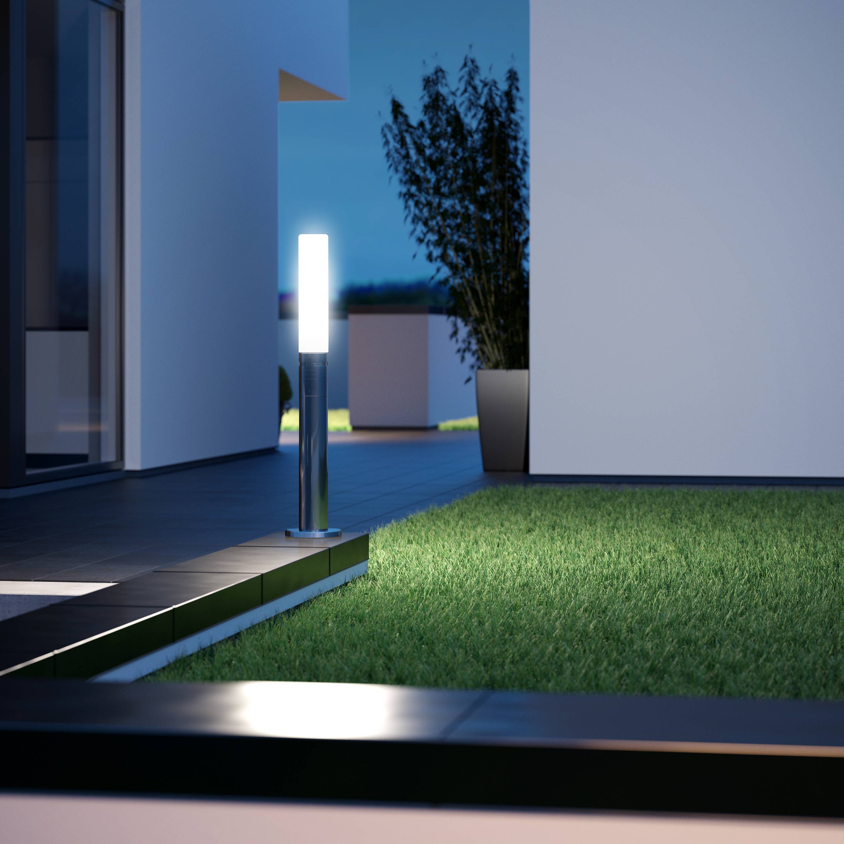 Eine beleuchtete moderne Terrasse mit Rasenfläche, bepflanztem Topf und minimalistischem Gebäude im Hintergrund bei Dämmerung.