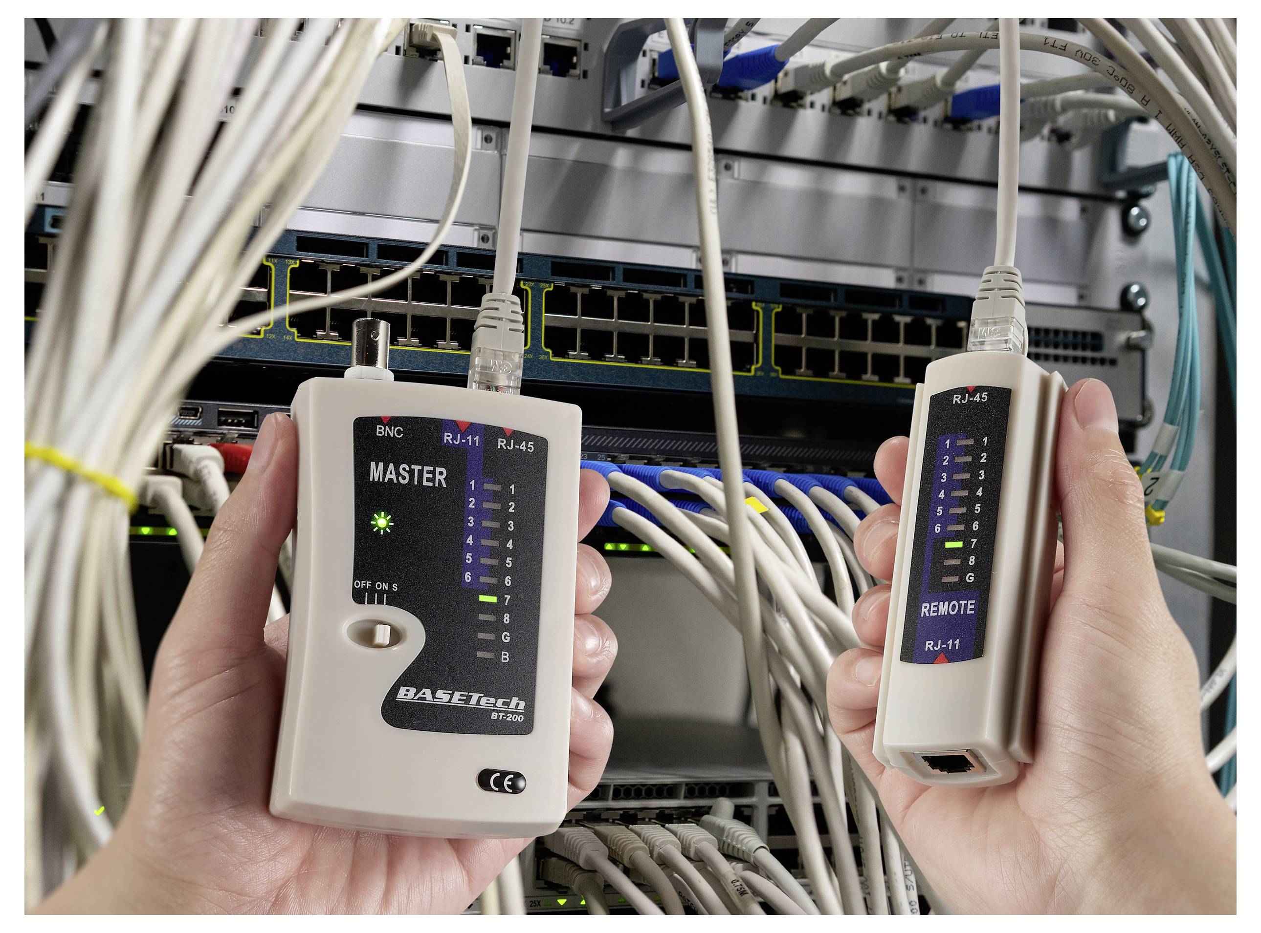 Hände halten ein Netzwerkkabel-Testgerät vor einem Serverrack, mit Kabeln, die mit Netzwerkausrüstung verbunden sind.