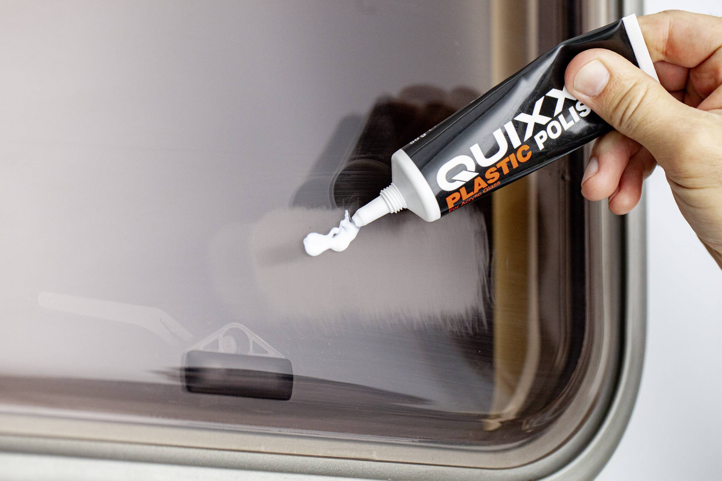Eine Hand drückt Politur aus einer Tube auf eine Kunststoffoberfläche, um Kratzer zu entfernen.