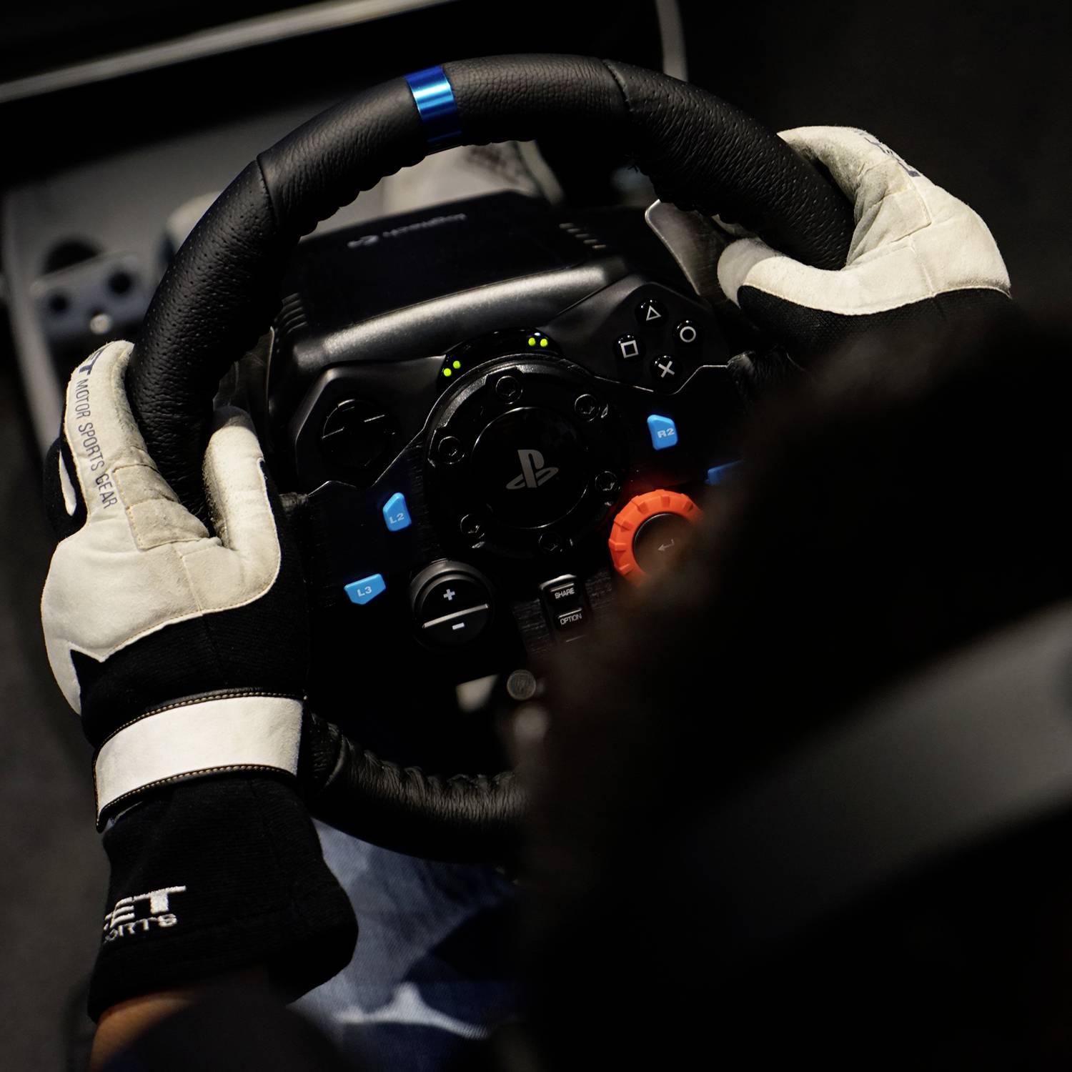 Eine Person mit Handschuhen hält ein Gaming-Lenkrad, das mit einem PlayStation-Logo versehen ist, bereit für eine Rennsimulation.