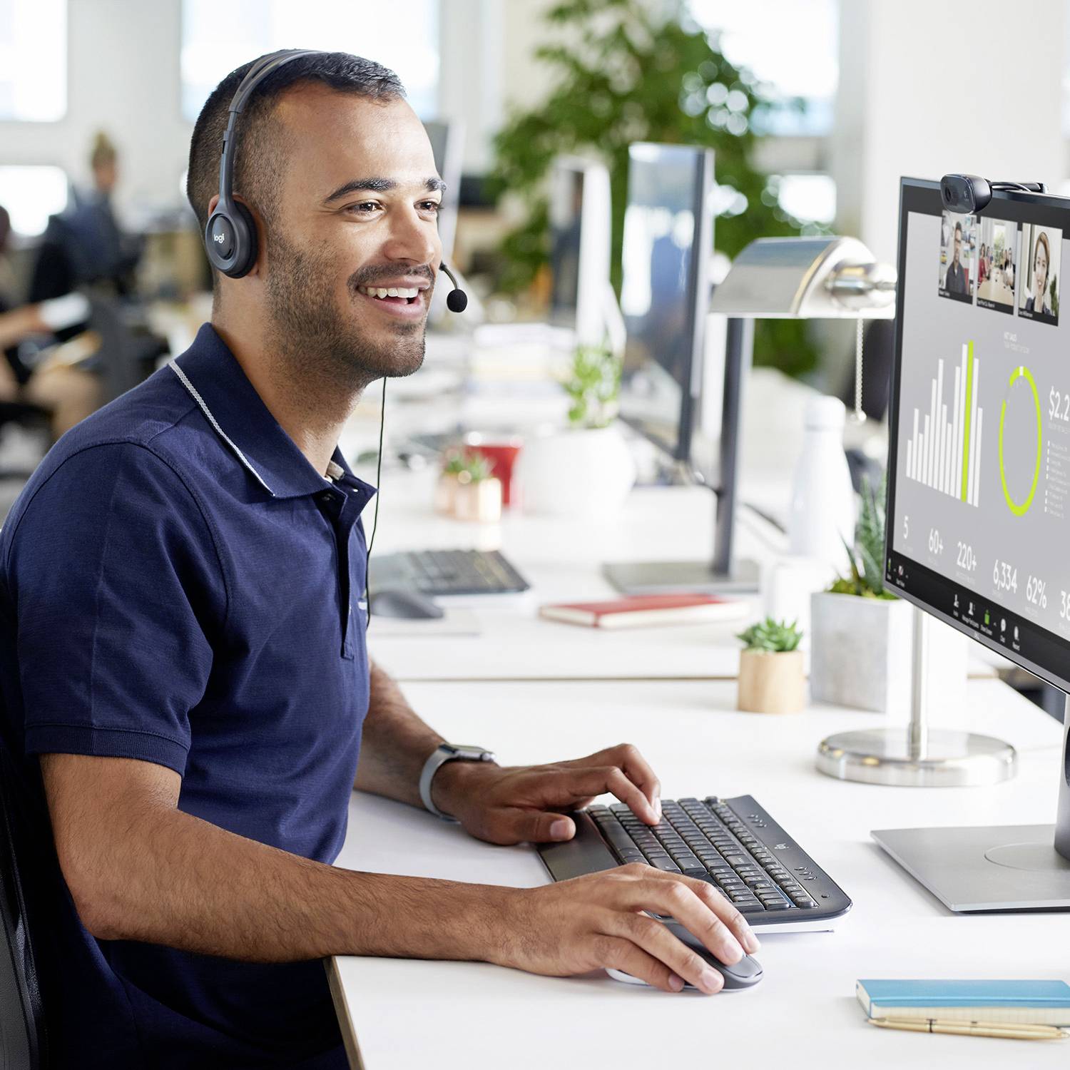 Mann mit Headset sitzt an einem Schreibtisch und tippt, während er auf einem Monitor Diagramme und Statistiken betrachtet. Büroarbeitsplatz.