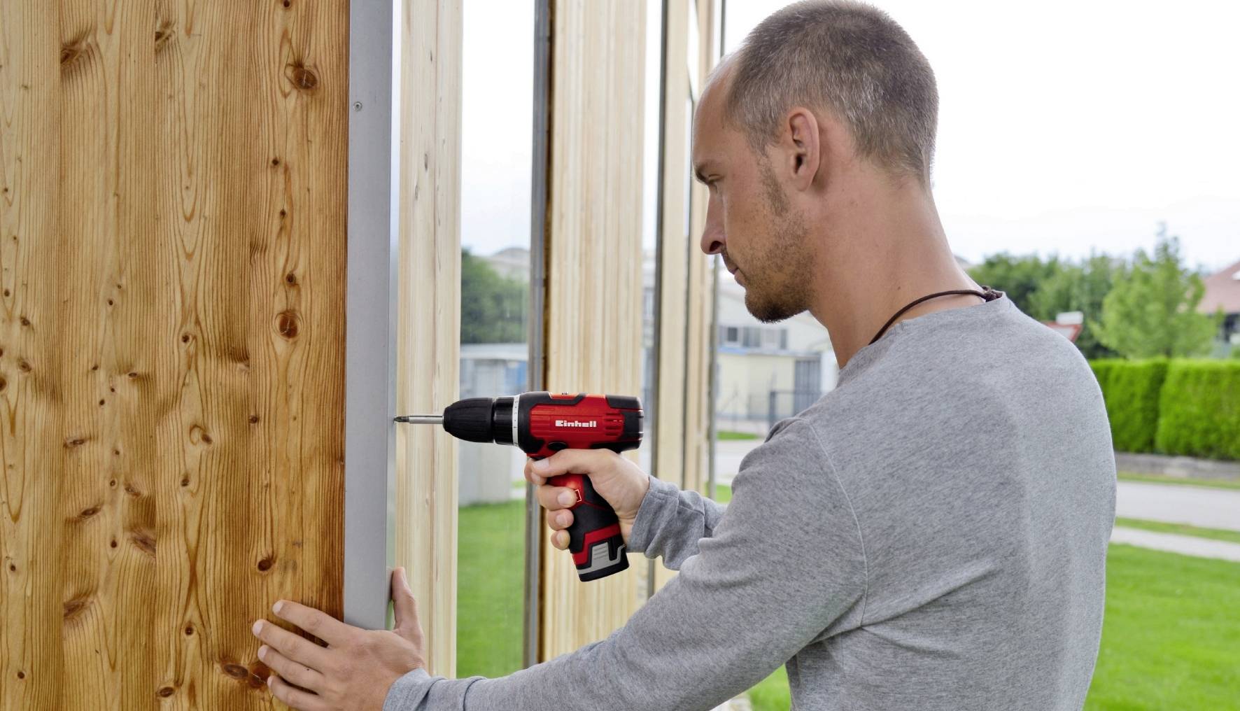 Ein Mann bohrt mit einer roten Bohrmaschine ein Loch in eine Holzpaneele.
