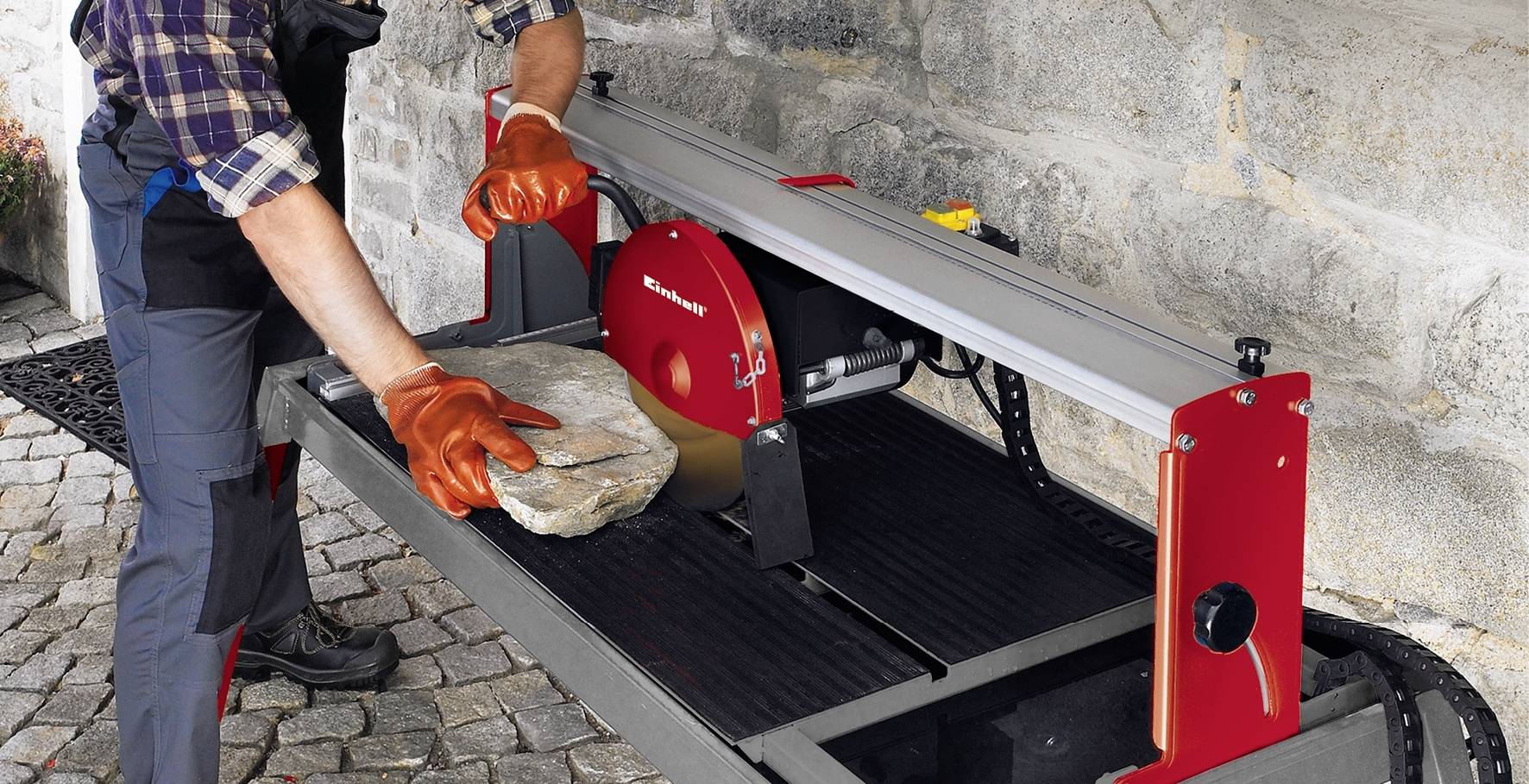 Eine Person schneidet mit einer Steintrennmaschine einen großen Steinblock. Die Maschine steht im Freien auf Pflastersteinen.