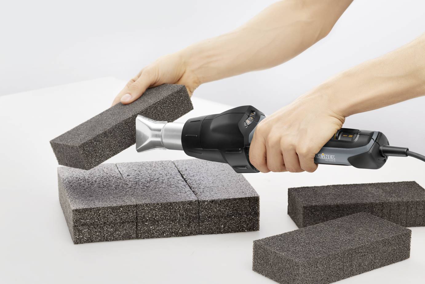 Person hält Heißluftgebläse, das auf Schaumstoffziegel gerichtet ist, um sie zu formen oder zu bearbeiten.