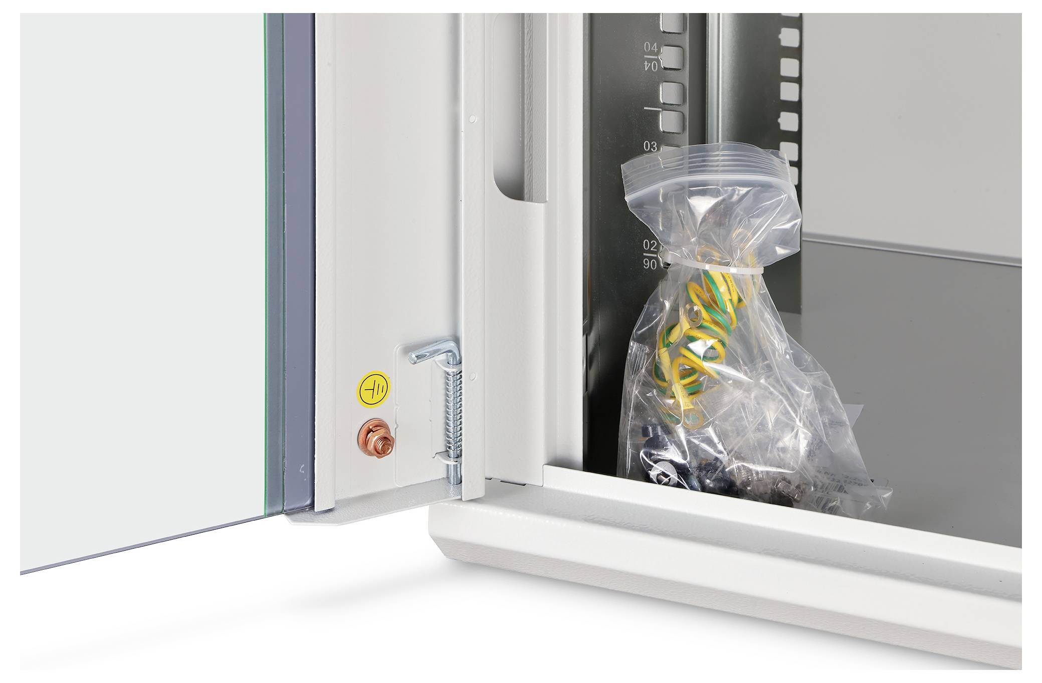 Eine offene Schranktür zeigt einen versiegelten Plastikbeutel mit gelben und schwarzen Kabeln im Inneren des Schranks. Ein Messmaßstab ist seitlich sichtbar.