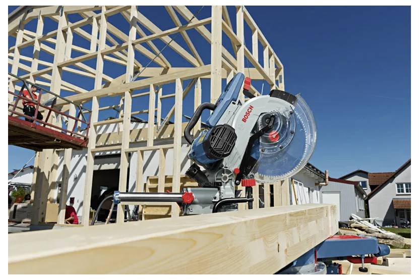 Eine Kreissäge schneidet einen Holzbalken auf einer Baustelle zum Hausbau unter klarem blauem Himmel.
