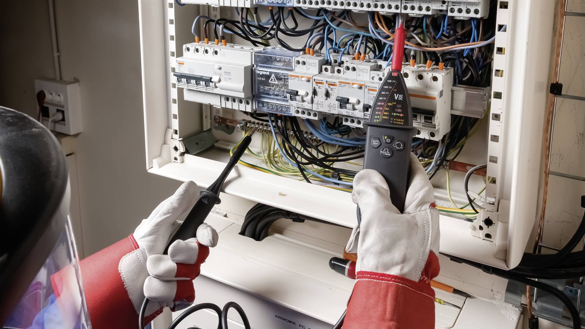 Elektriker trägt Schutzausrüstung und überprüft elektrische Schaltanlage mit Messgeräten.