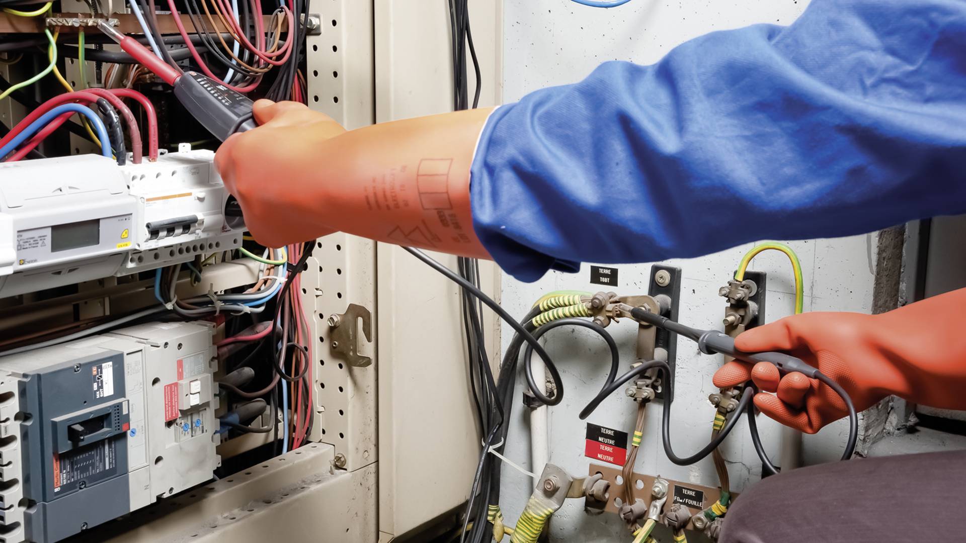 Eine Person in Schutzkleidung arbeitet an einem offenen Schaltschrank mit vielen Kabeln, überprüft die elektrischen Verbindungen.