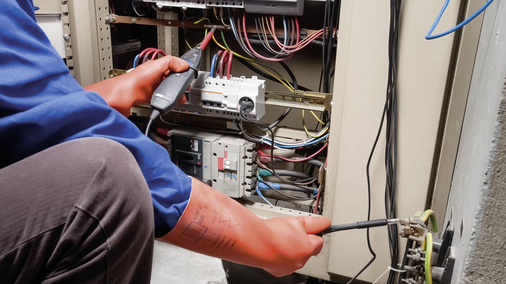 Ein Elektriker in blauer Kleidung arbeitet mit Werkzeug an einem Schaltschrank voller Kabel und Komponenten zur Reparatur oder Wartung.