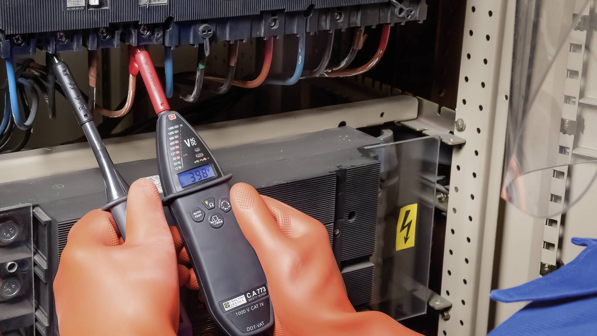 Ein Techniker misst die Spannung in einem Schaltschrank mit einem Multimeter. Er trägt Sicherheitshandschuhe.