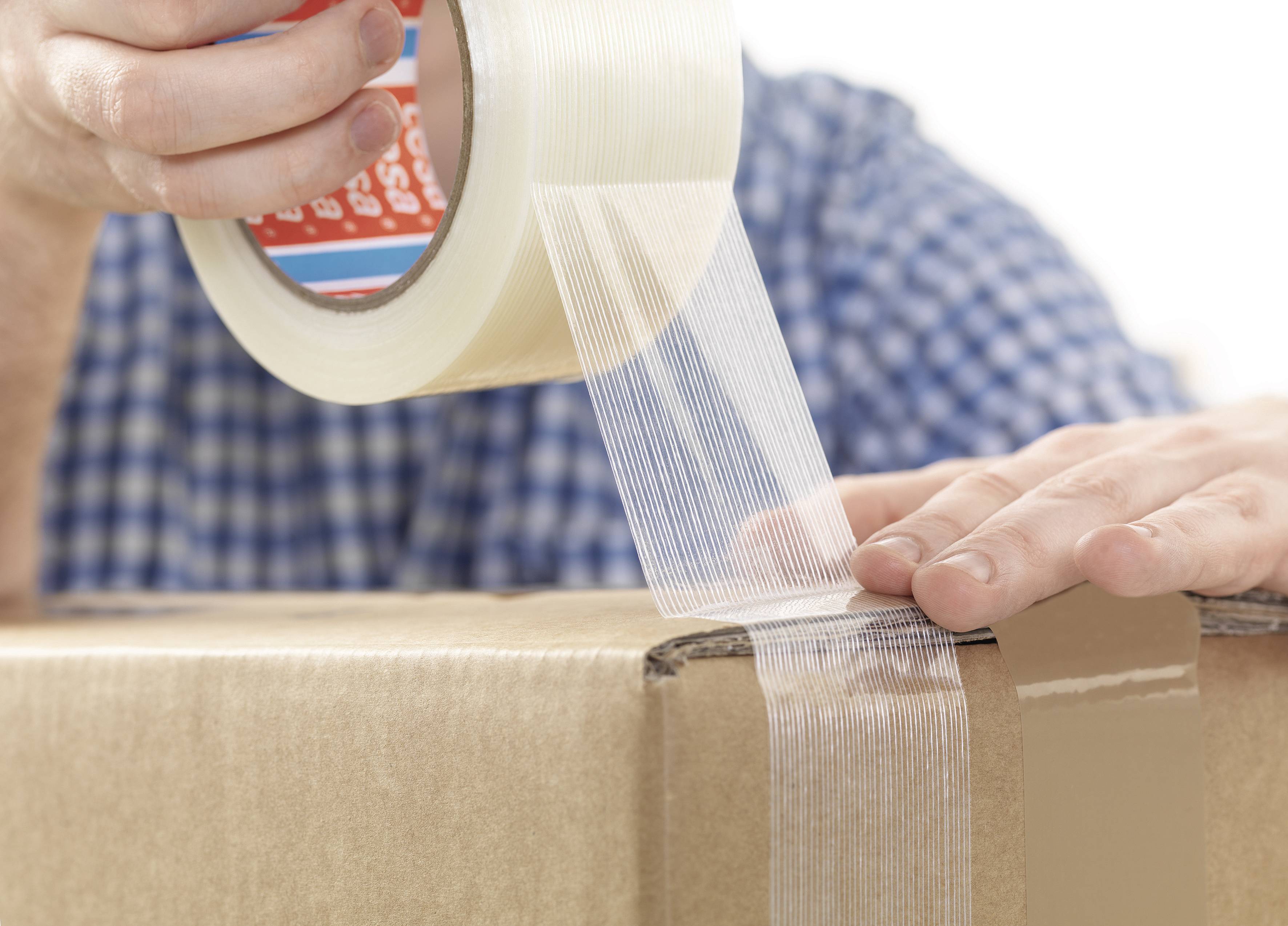 Person verpackt einen Karton mit durchsichtigem Klebeband. Die Person trägt ein kariertes Hemd.