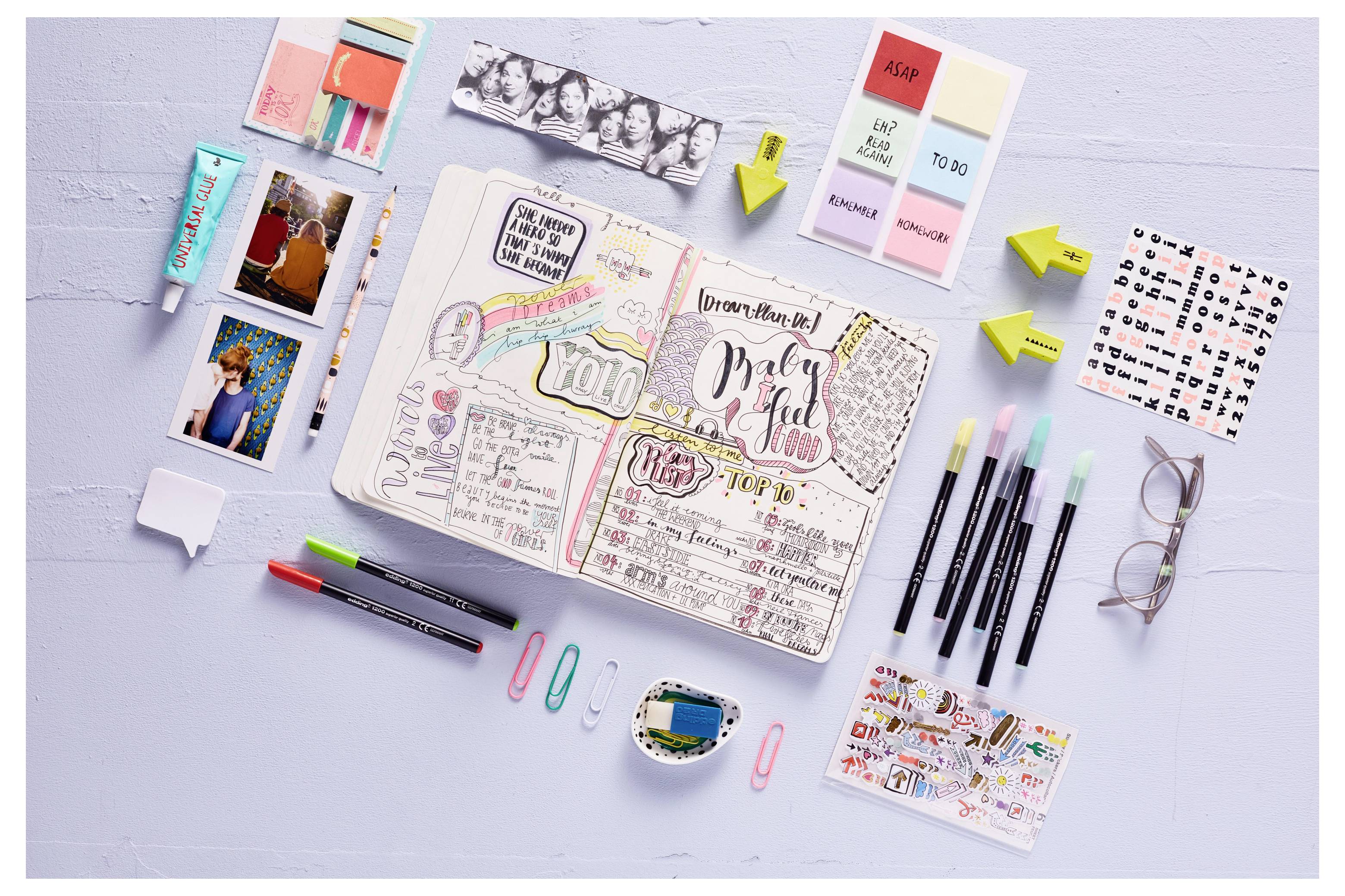 Aufgeschlagenes Bullet-Journal mit farbenfrohen handgezeichneten Notizen und 'Babyparty'-Schriftzug, umgeben von Stiften, Haftnotizen, Fotos, Clips und Aufklebern.