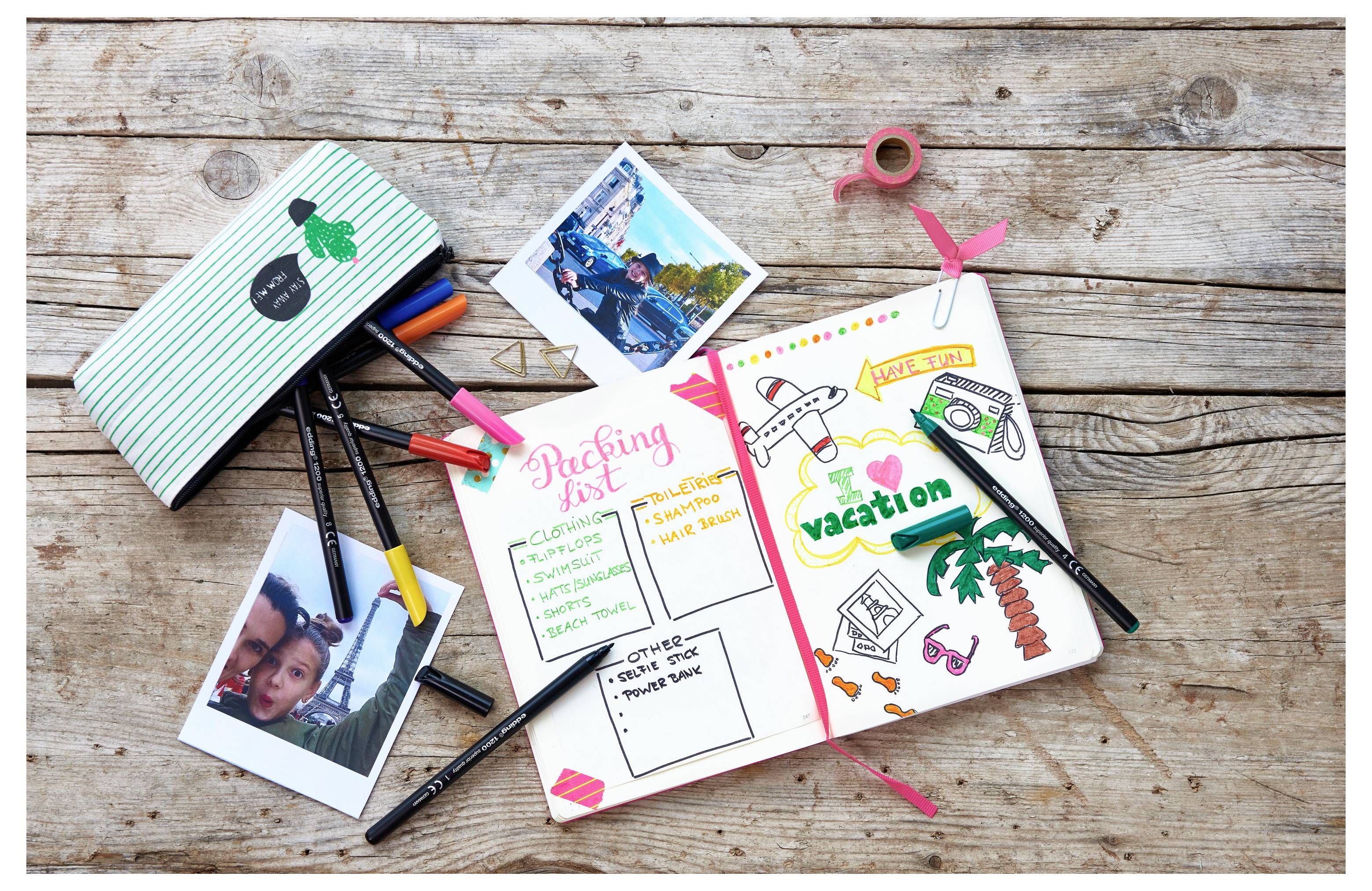 Eine Reisejournal-Szene mit einem offenen Scrapbook, dekorierten Urlaubsseiten, Fotos, Stiften, Notizbuch und Washi-Klebeband auf einem Holztisch.