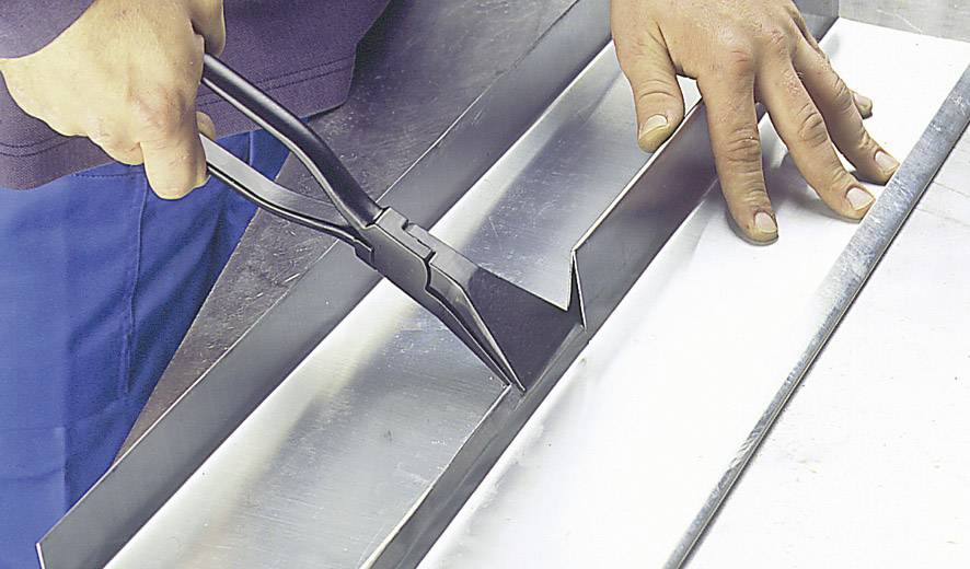 Eine Person biegt ein Metallblech mit einer Handbiegemaschine. Die Szene zeigt Handwerk und präzise Metallbearbeitung.