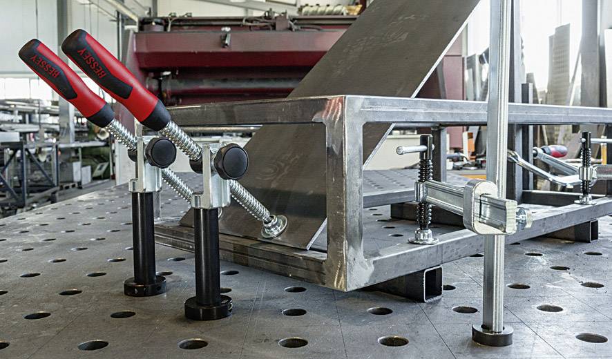Metallwerkstatt mit fixiertem Metallrahmen auf einem Lochblechtisch. Mehrere Klemmen halten den Rahmen während der Bearbeitung.