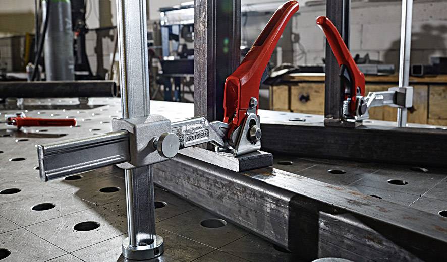 Metallwerkstatt mit Spannwerkzeugen auf einem Lochblechtisch; im Hintergrund weitere Werkzeuge und Geräte erkennbar.