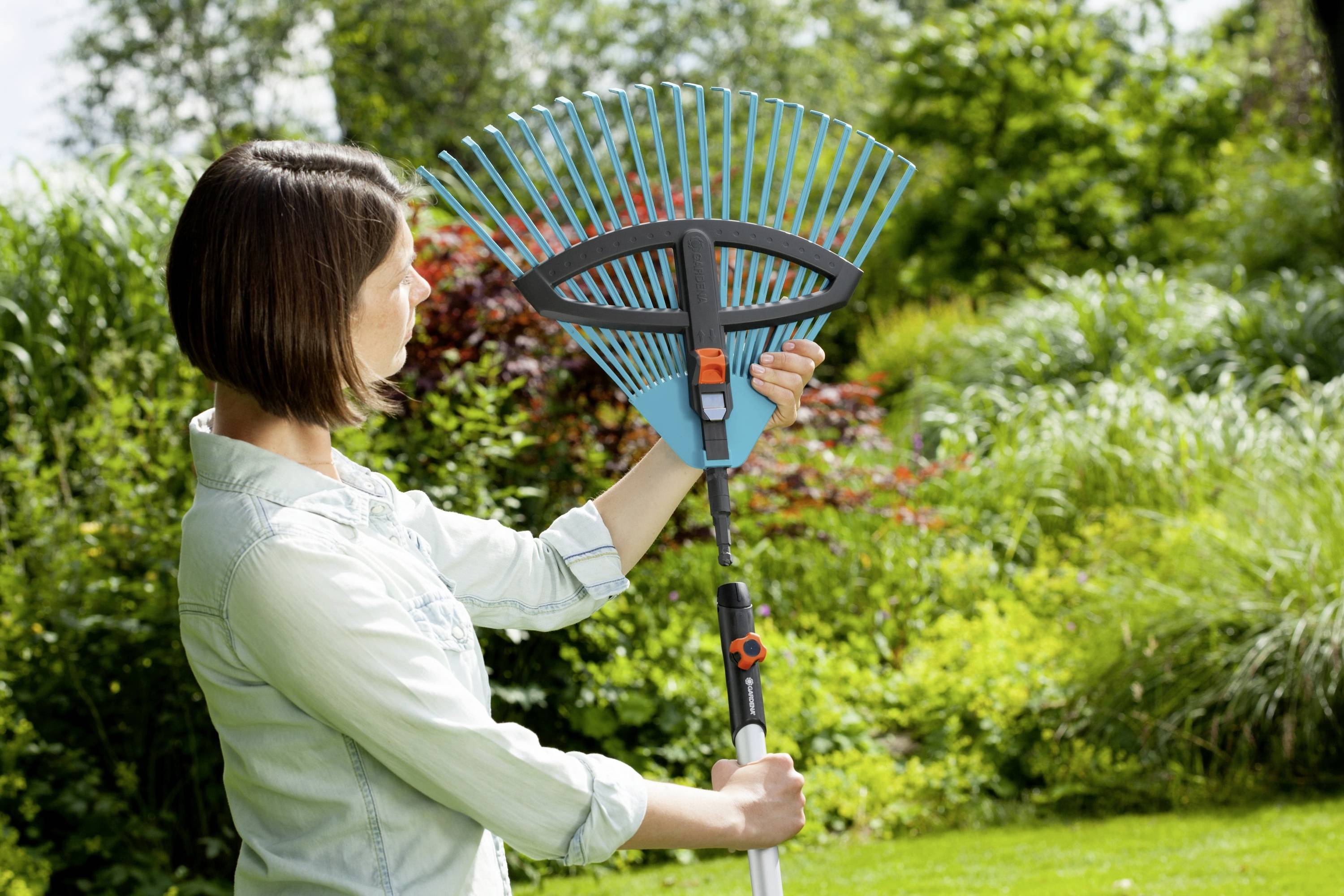 Person hält einen verstellbaren Rechen im Garten. Umgeben von grünem Laub und Pflanzen. Sie überprüft die Werkzeugeinstellung.