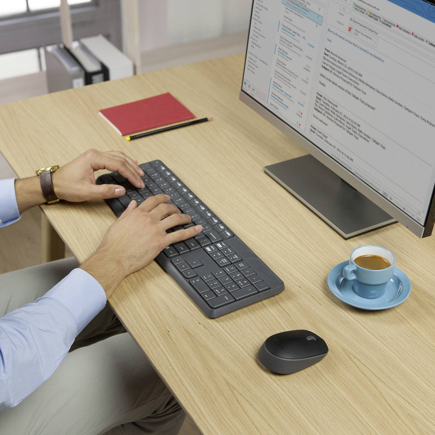 Eine Person tippt an einem Schreibtisch auf einer Tastatur. Daneben stehen eine Tasse Kaffee, ein Notizbuch und ein Computerbildschirm.