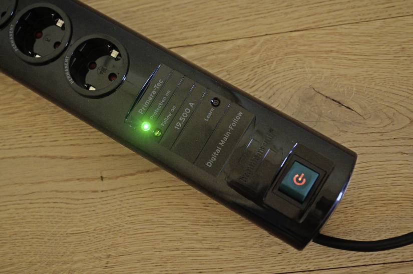 Steckdosenleiste mit grünem Licht auf Holzboden, anzeigend, dass der Strom eingeschaltet ist.