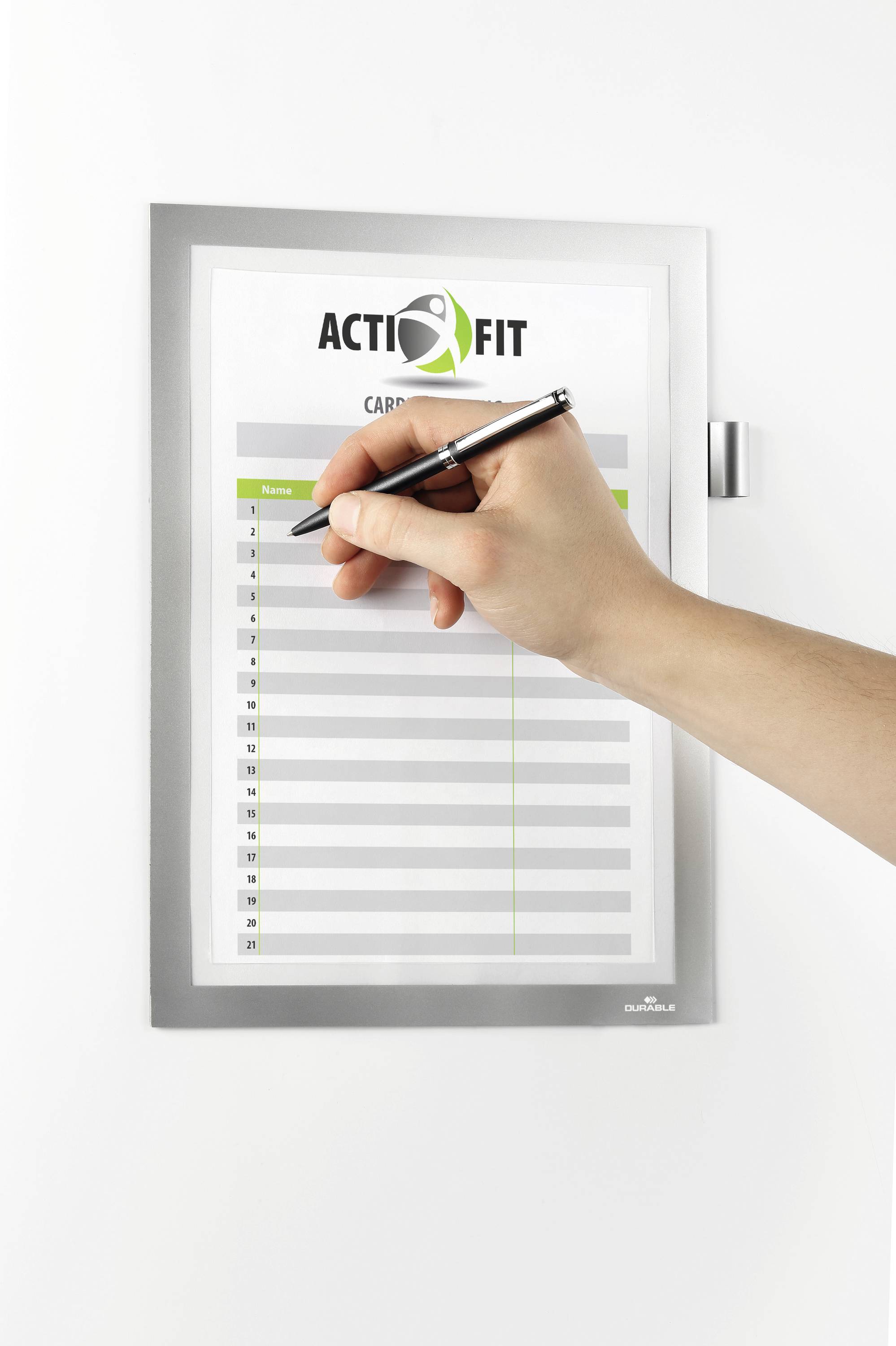 Ein Stift markiert eine Aktivitätsliste mit dem Titel 'ACTIFIT CARDIO'. Die Liste hat Spalten für Namen und Daten, befestigt an einer Wand.