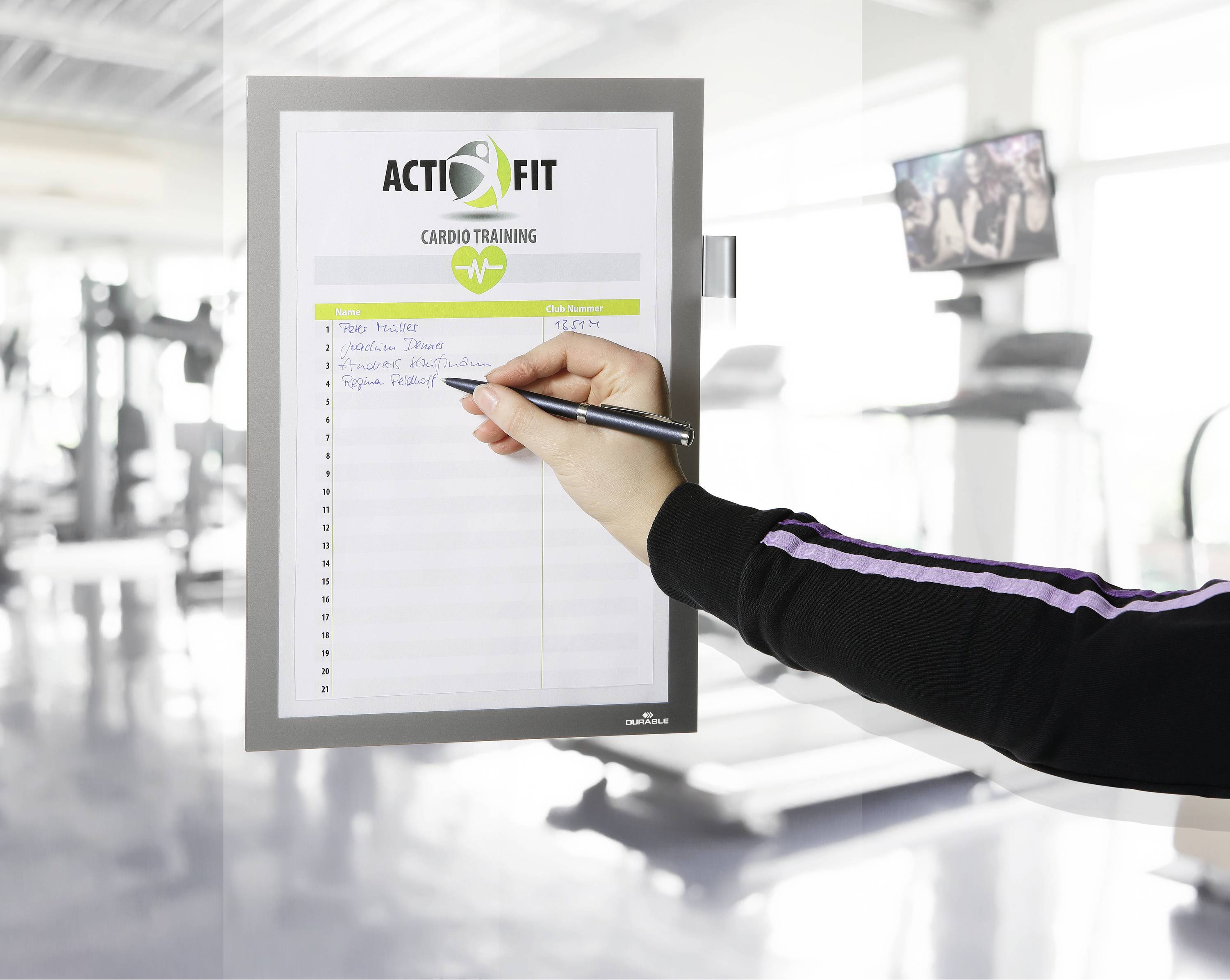 Eine Person schreibt mit einem Stift auf ein Formular mit der Überschrift 'ACTIFIT Cardio Training' in einem Fitnessstudio.
