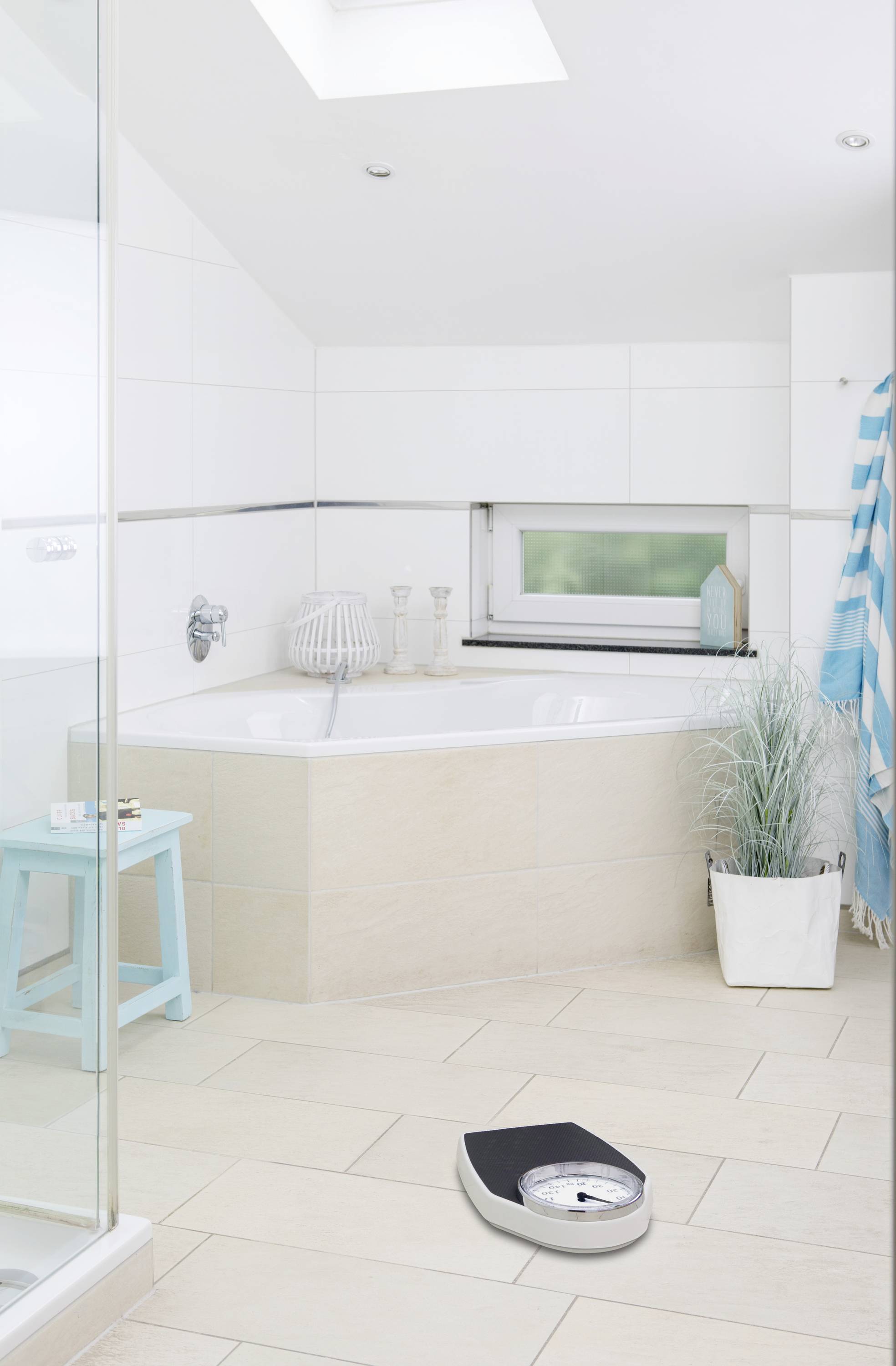 Modernes Badezimmer mit Badewanne, Fenster, blauen Akzenten, Topfpflanze und Personenwaage auf dem Boden.
