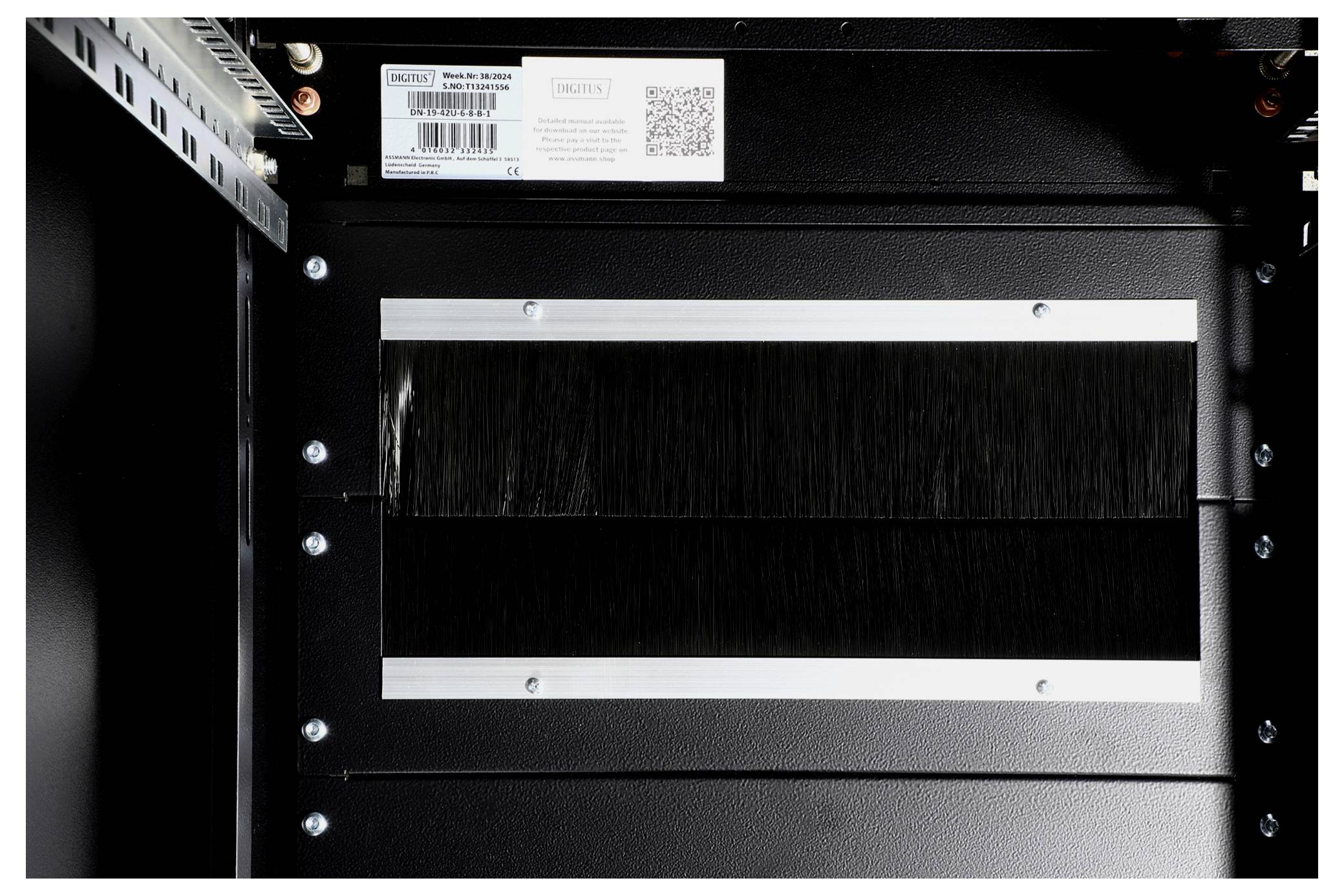 Metallplatte mit Kabeldurchführung und Bürstendichtung in einem schwarzen Gehäuse. Oben ein Typenschild mit QR-Code und CE-Kennzeichnung.