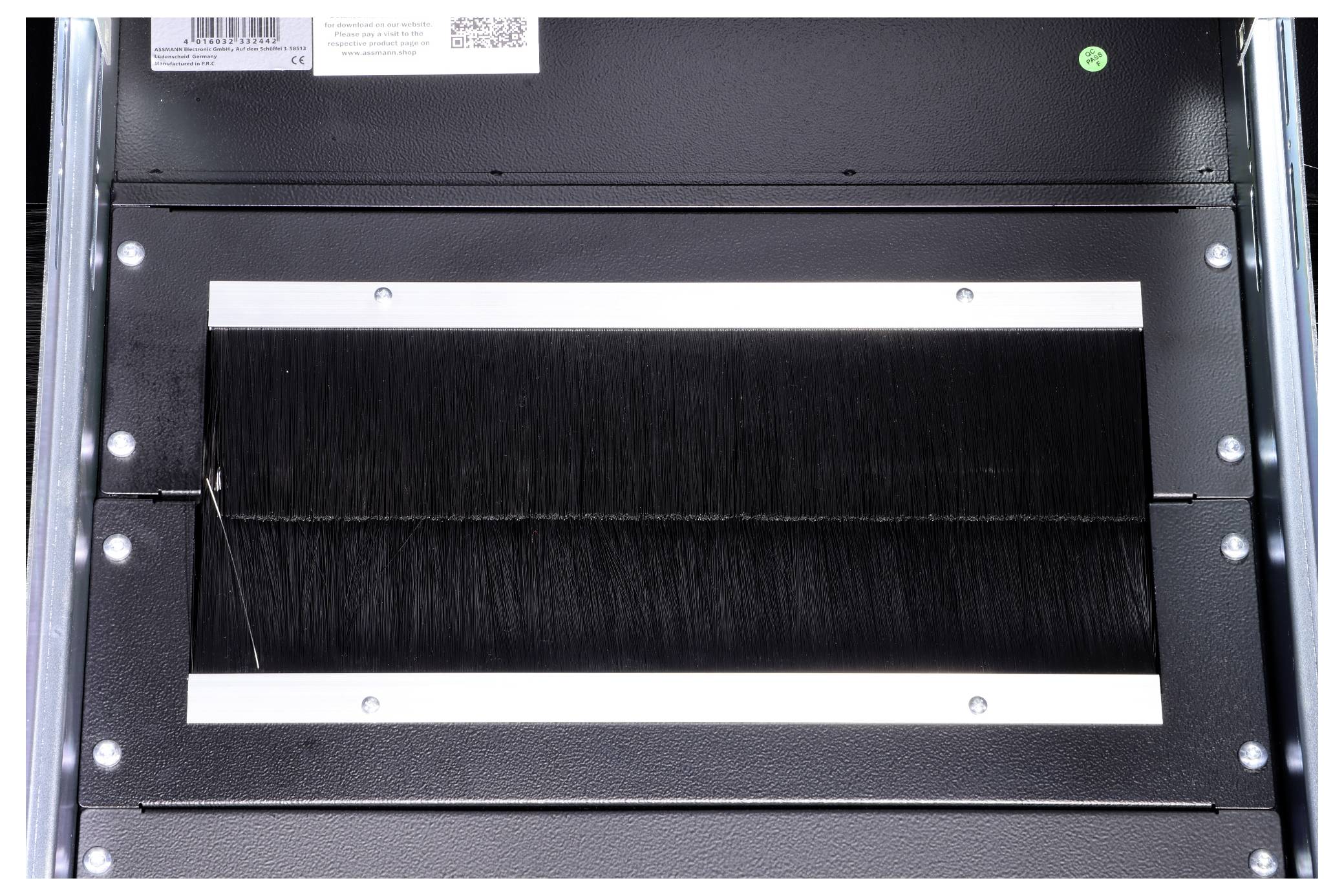 Die Abbildung zeigt eine schwarze Bürstenleiste in einem rechteckigen Metallrahmen, die als Schutz oder Führung in einem Gerät dient.