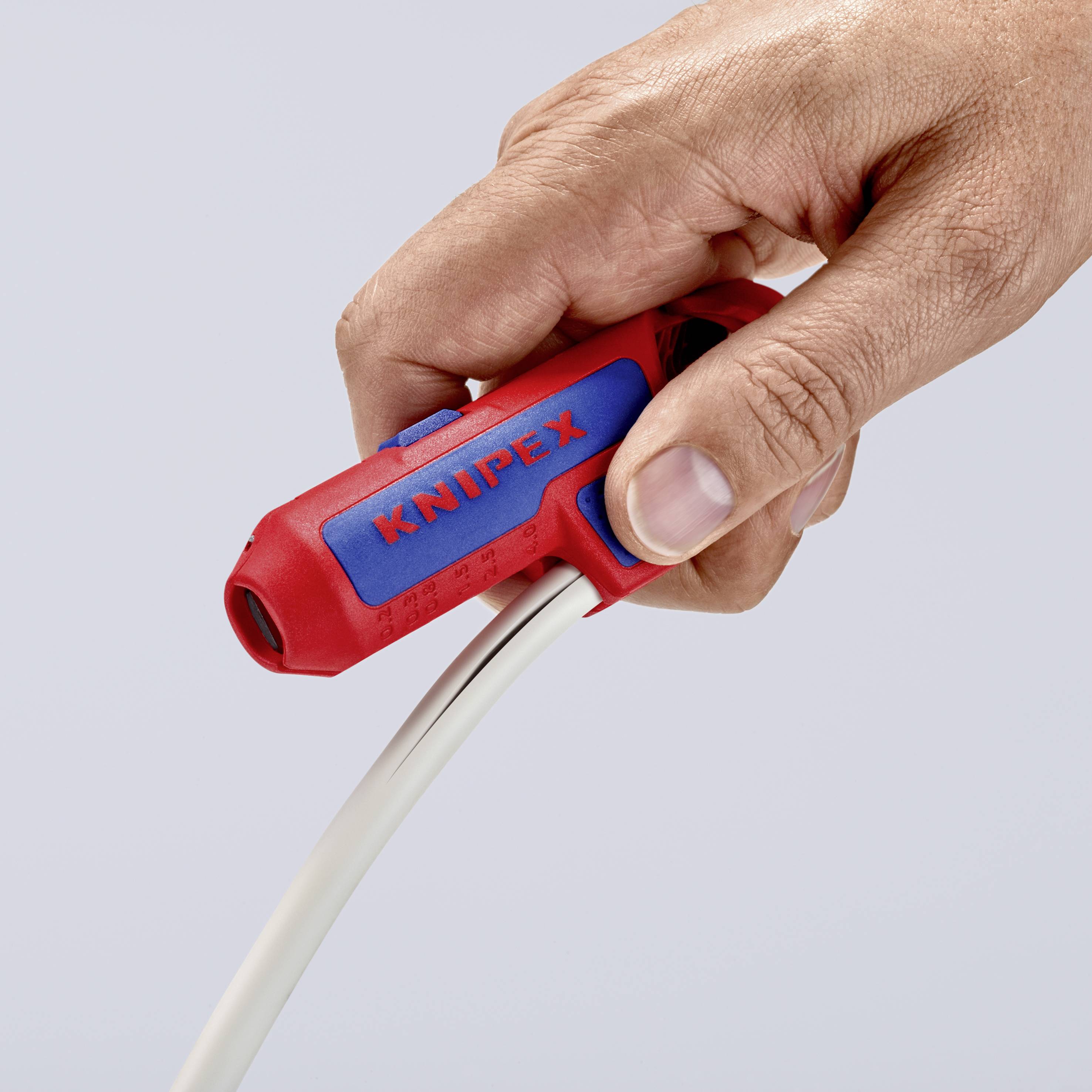 Hand hält einen roten Kabelschneider mit blauem Logo, schneidet ein weißes Kabel. Fokus auf Werkzeug und Handhabung.