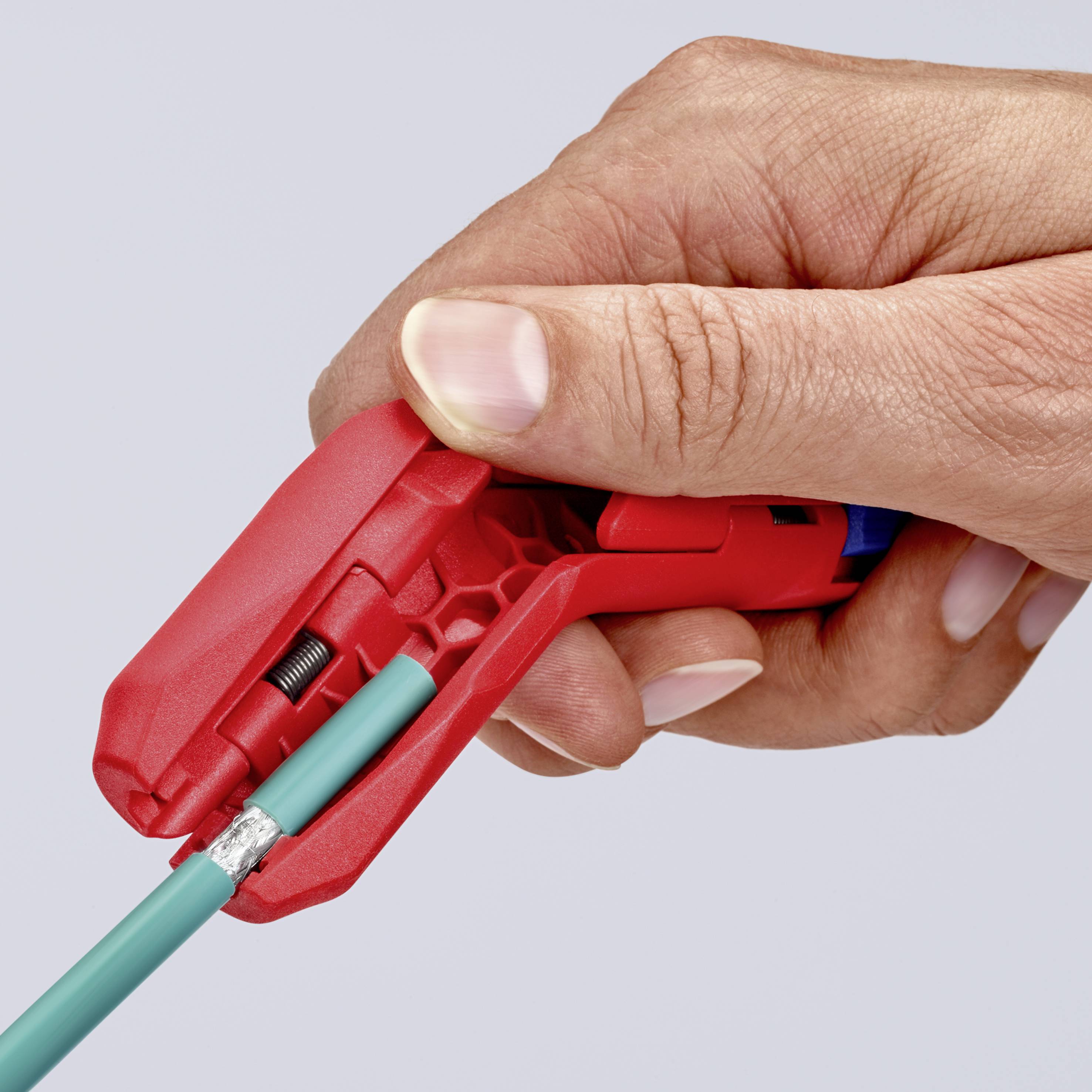 Hand hält ein Abisolierwerkzeug, das ein rotes Kabel abschneidet. Das Bild zeigt den Abisolierprozess in Aktion.