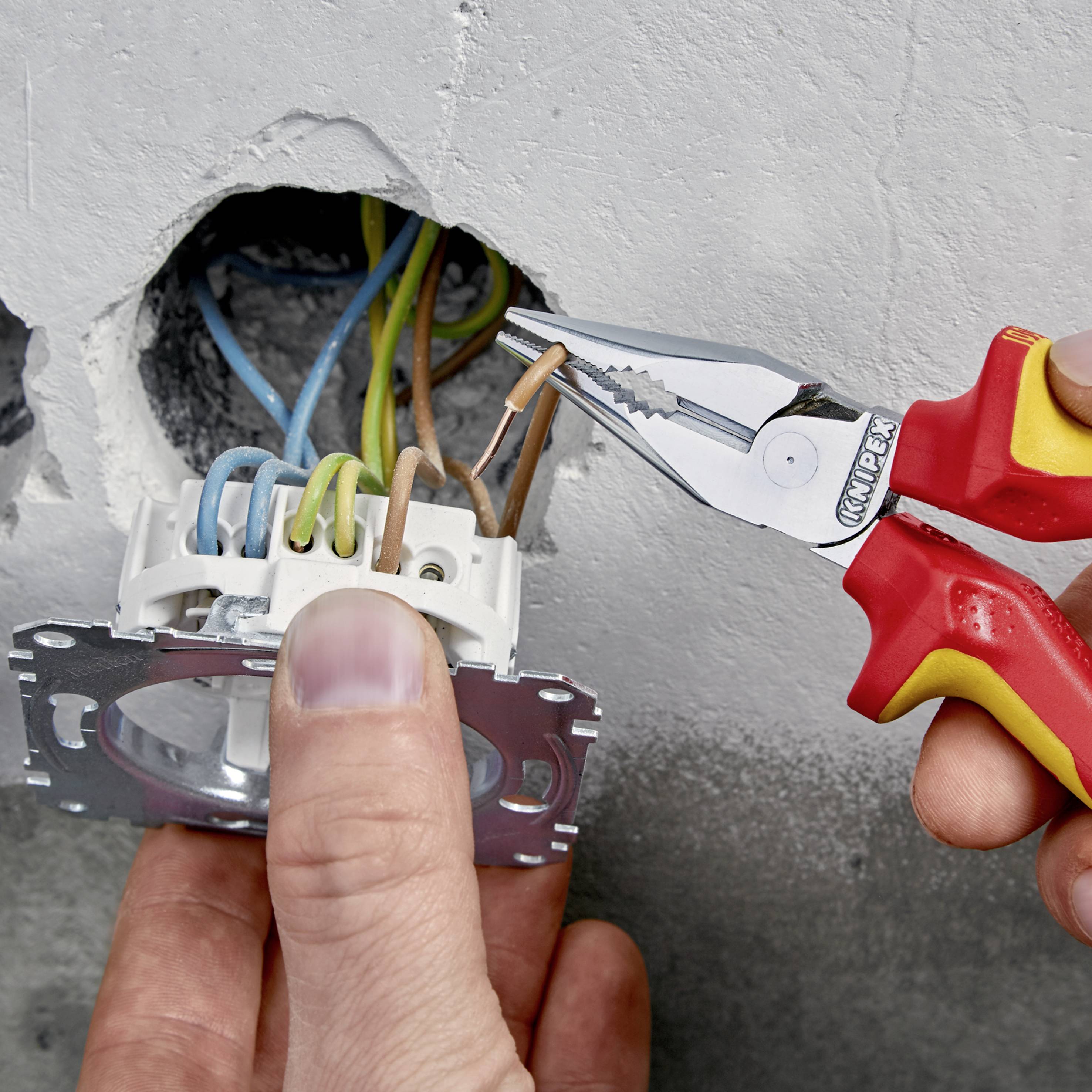 Ein Handwerker installiert eine Steckdose, verwendet eine Zange zum Klemmen der Kabel, die aus der Wand herausgeführt sind.